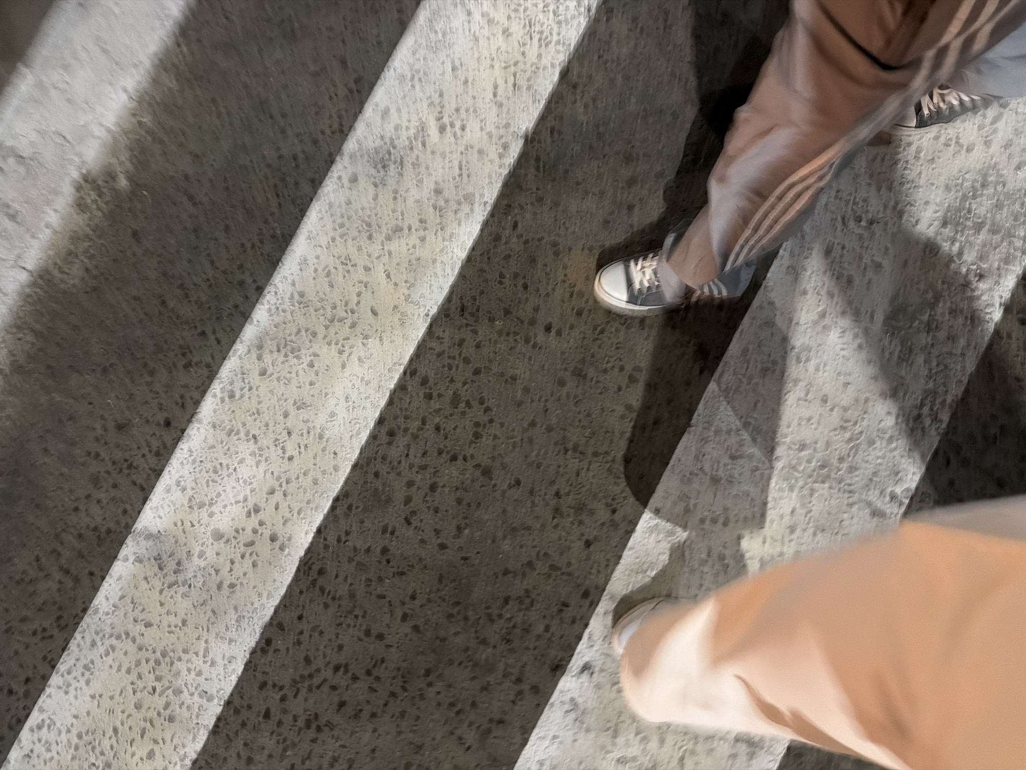 The image depicts a set of concrete stairs, possibly outdoors, with two people walking on them. One person is wearing gray sneakers with white laces and gray pants with three white stripes down the side. The other person appears to be wearing light-colored pants. The stairs have a light gray and dark gray speckled pattern.
Without additional details from the image itself, determining a specific location in Izhevsk, Russia is impossible.
