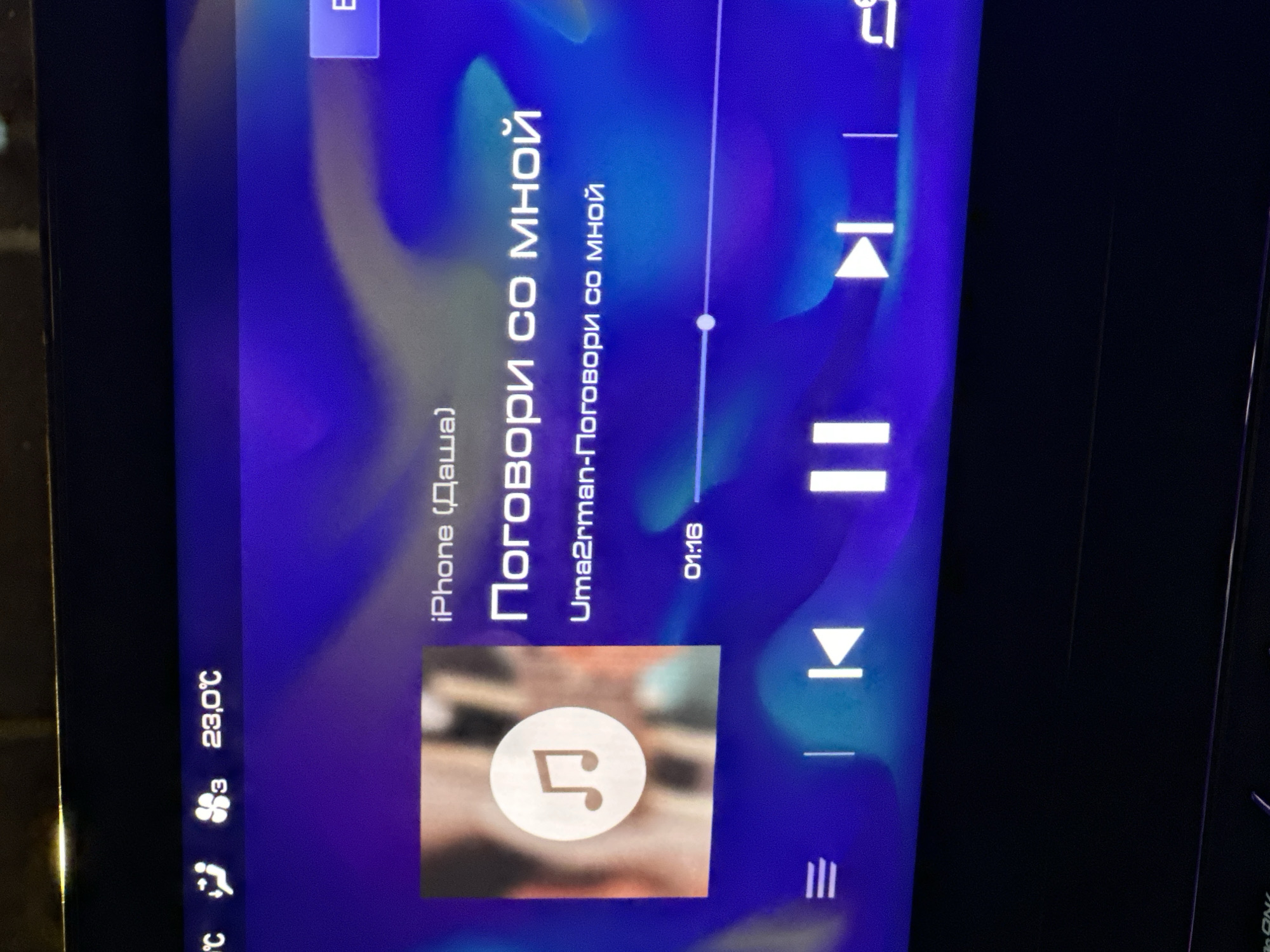 The image depicts a screen displaying audio playback information. The audio is playing from an iPhone (named "Даша"), and the song title is "Поговори со мной" (Talk to Me), by Uma2rman. The song's playback time is at 01:16. The screen also shows the temperature is 23.0℃. The location is likely inside a vehicle, given the context of audio playback and temperature display. No additional information indicates the scene being in Moscow.