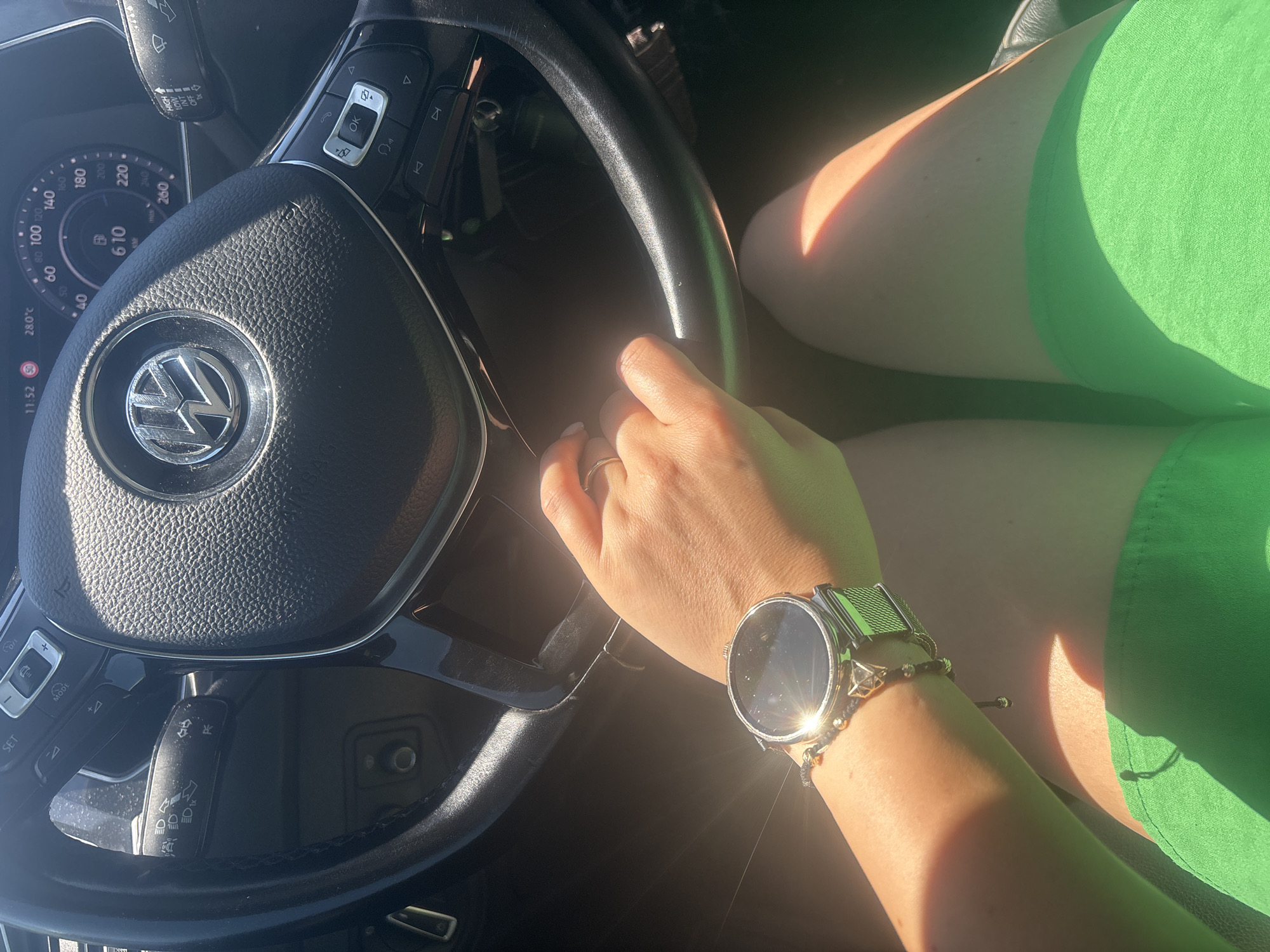 The image shows a first-person perspective of someone driving a car in Burgas, Bulgaria. The driver's hands are on the steering wheel, and a smartwatch is visible on their left wrist. The car's dashboard and a portion of the road are also visible. The lighting suggests it is daytime, possibly with bright sunlight. The driver is wearing green shorts.