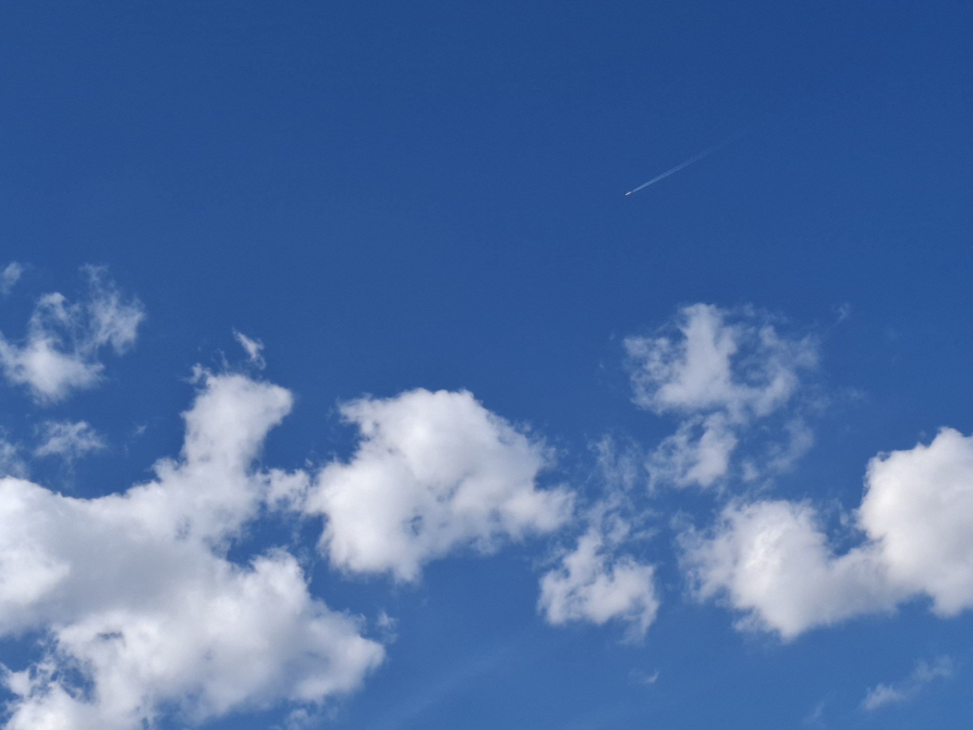 The image shows a blue sky with white clouds and a contrail from an airplane. The clouds are mostly concentrated in the lower half of the image. The contrail is in the upper right quadrant. The location is not discernible as Zverino, Bulgaria.
