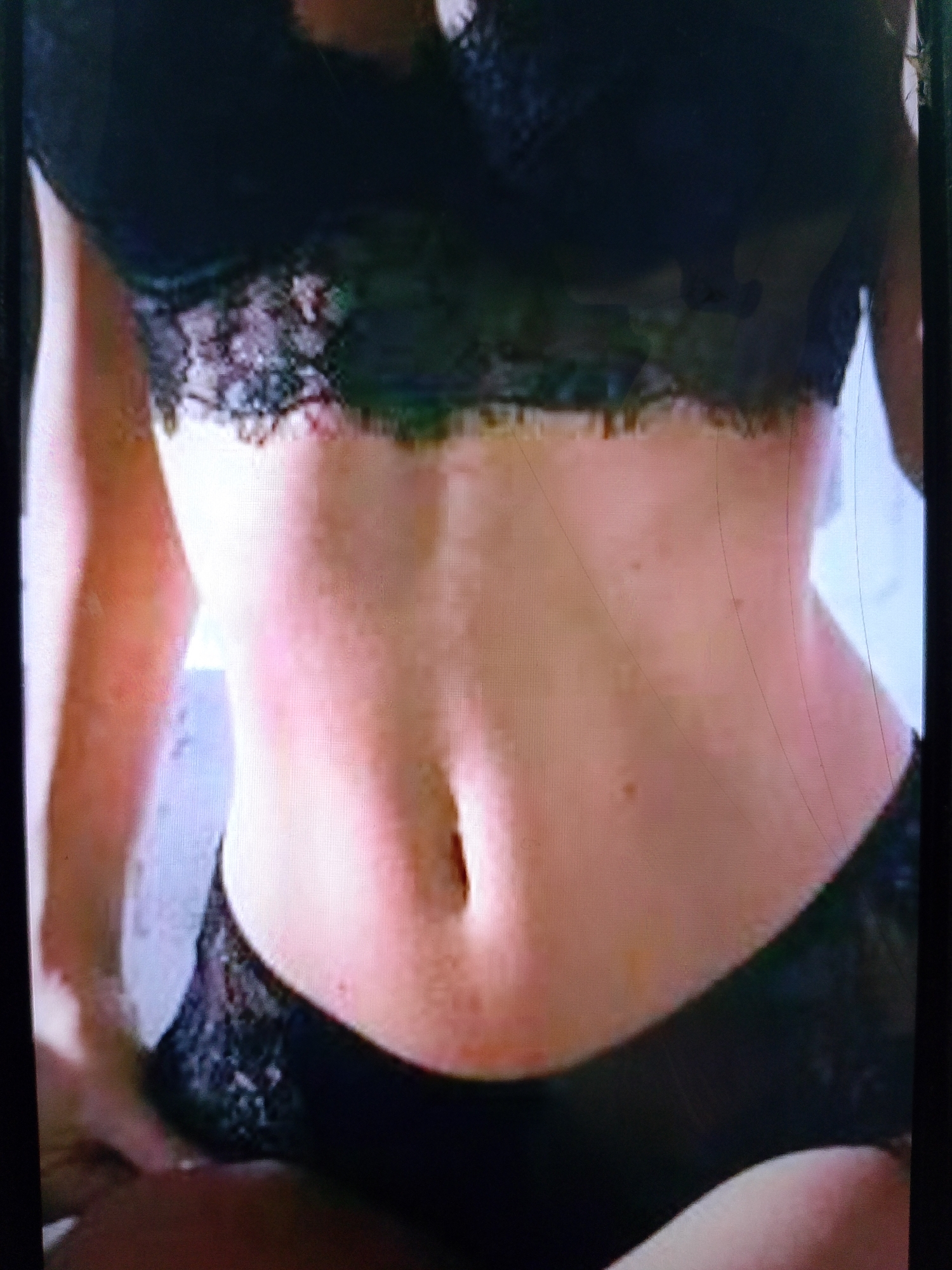 The image shows a close-up view of a person's torso, wearing black lace lingerie. The focus is on the midriff and the lower part of the breasts. The person's skin is visible, with some freckles or marks. The background is indistinct and appears to be an indoor setting. There is no visible indication of the city of Dobra Krynytsia, Ukraine, or any elements that would suggest this location.
