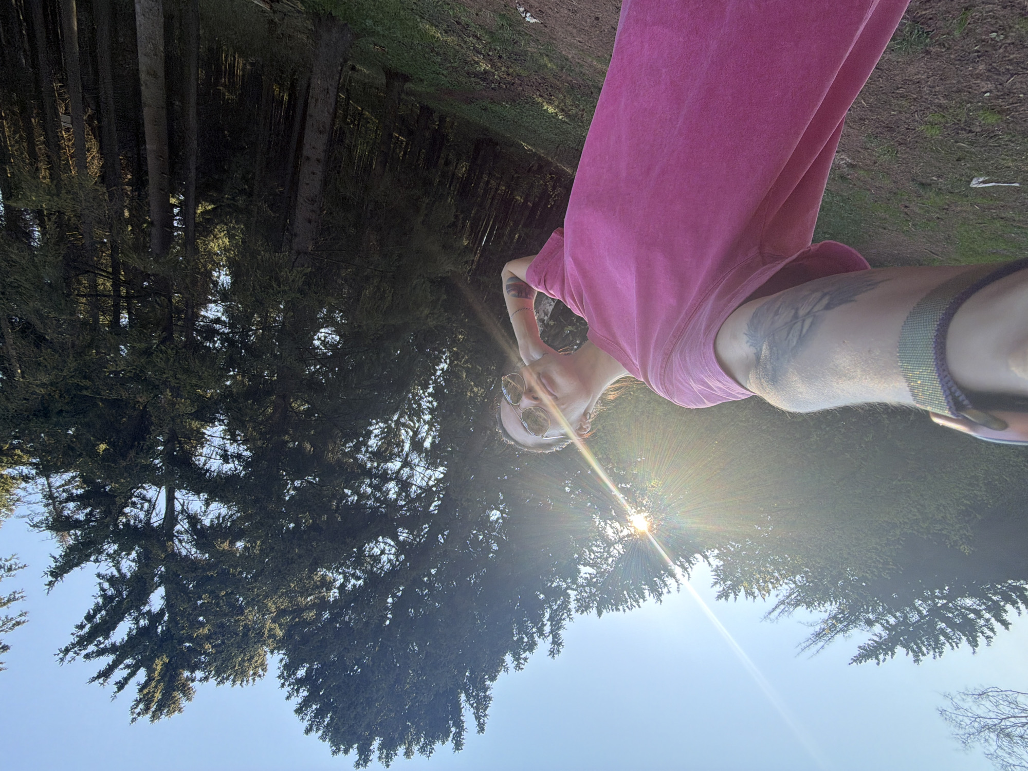 A person wearing a pink shirt and sunglasses is taking a selfie outdoors in a wooded area. Sunlight is visible through the trees. The location is unspecified, and there is no information available about the city of Perm, Russia.