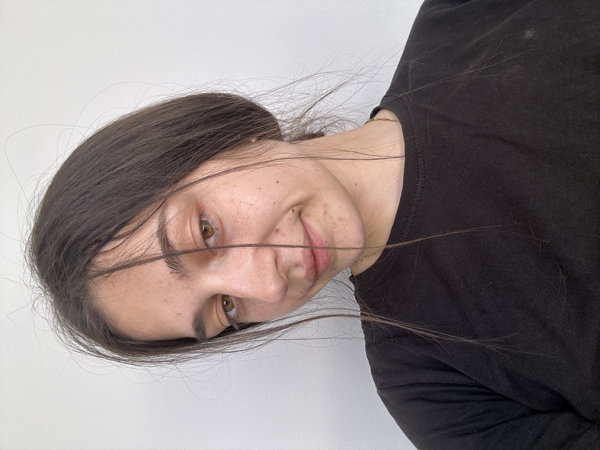 A young woman with brown hair and freckled skin is looking at the camera. She has light brown eyes and a slightly smiling expression. She is wearing a black shirt. The background is a plain white wall. There is no indication of the city of Resen, Bulgaria, or any specific location.