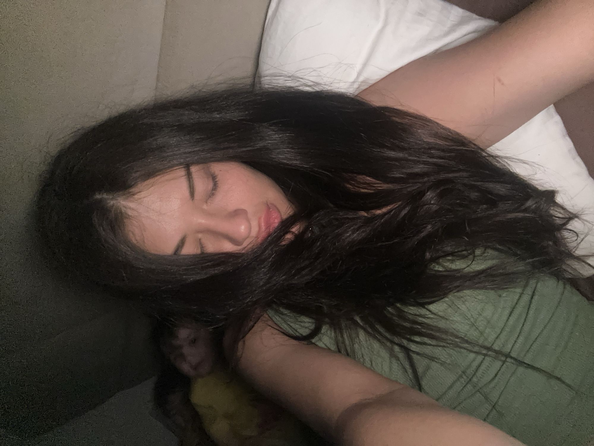 A person is lying on their side on a bed or couch. They have long, dark hair and are wearing a green shirt. A white pillow is visible behind the person's head. The person's eyes are closed, suggesting they are sleeping. It is not possible to determine a location in Khimki, Russia, from this image.