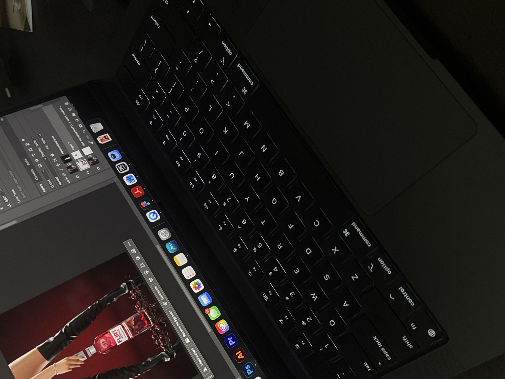 A laptop is open, displaying an image of a "FLIRT" vodka bottle with hands and legs in a red-toned background. The laptop screen also shows editing software with various tools and layers. The laptop keyboard is visible, with illuminated letters. The image shows the open computer, but it is difficult to ascertain the precise location in Sofia, Bulgaria from it.