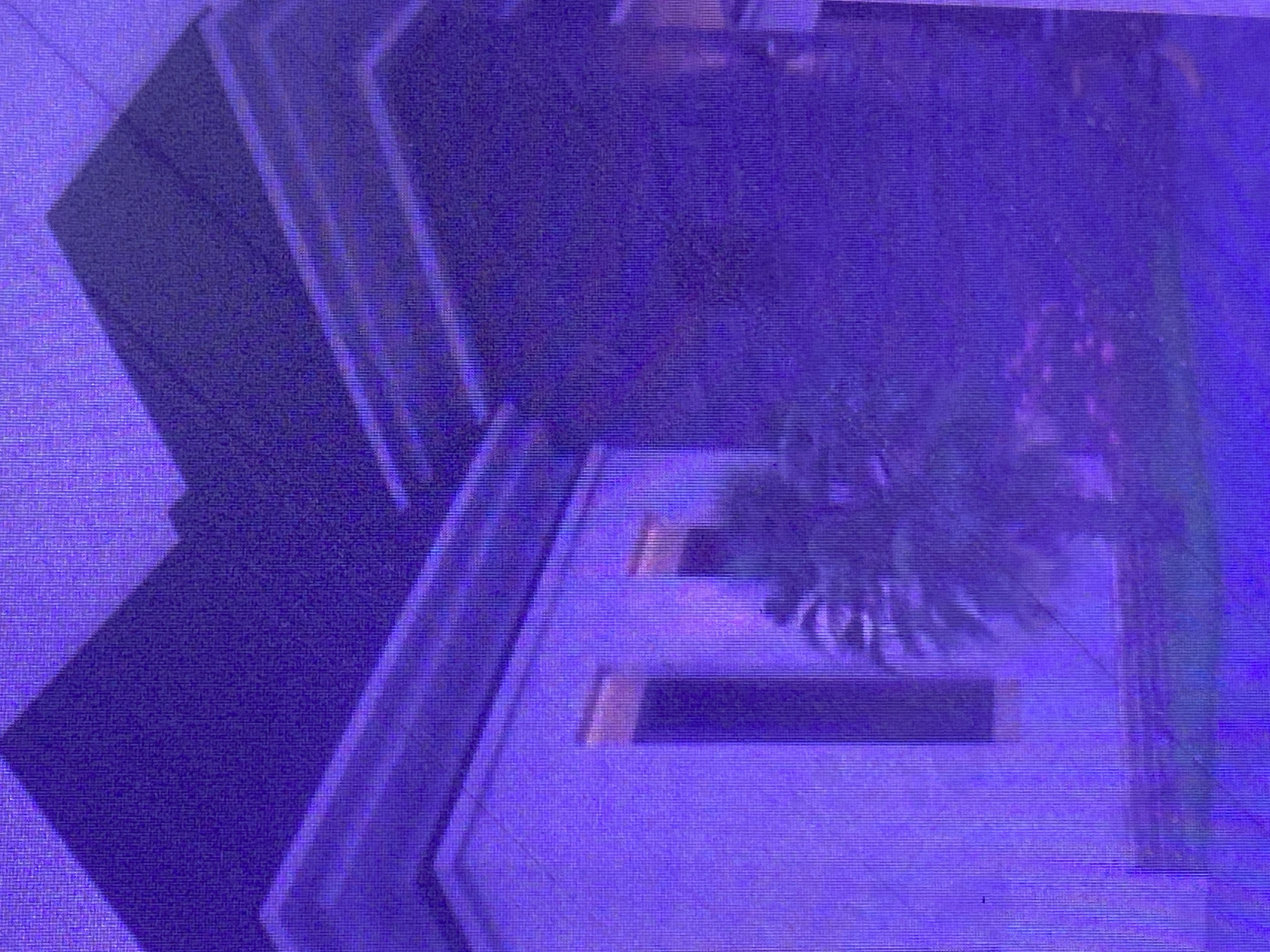 This image, taken in Ikorodu, Nigeria, displays a digitally rendered scene with a distinct purple hue. The scene appears to be an abstract architectural design or a stylized representation of an outdoor space. Geometric shapes, possibly suggesting steps or layered platforms, dominate the left side of the frame. These shapes are rendered in dark purple and a lighter, almost luminous purple.
On the right side, a shadowy, indistinct object suggests the presence of vegetation, perhaps a stylized tree or bush, also cast in shades of deep purple. There are rectangular elements within the platforms, one appearing darker than the other, which could represent inlays or recessed areas. The overall impression is one of a futuristic or artistic interpretation of a physical environment. The image lacks any discernible people, specific weather conditions, or clear time-of-day indicators. There is no visible text in the image. The digital nature of the image is evident from the pixelated quality and the uniform, almost unnatural coloring.
