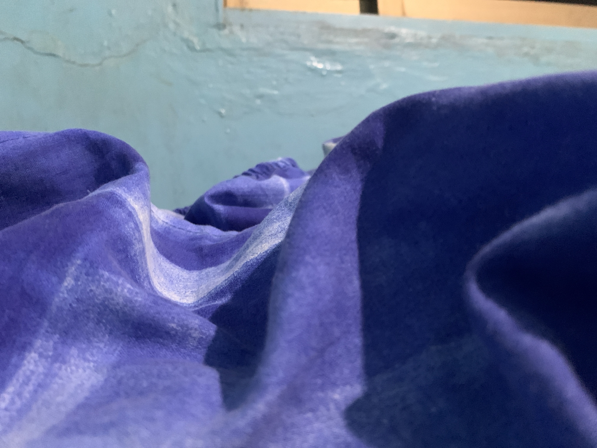 The image shows a close-up of draped blue and white fabric, possibly a bedsheet, in a room with light blue walls. The light source appears to be coming from a window in the upper portion of the frame.
I cannot provide the location in the city of Santa Ana, Venezuela, as there is no location information in the image.