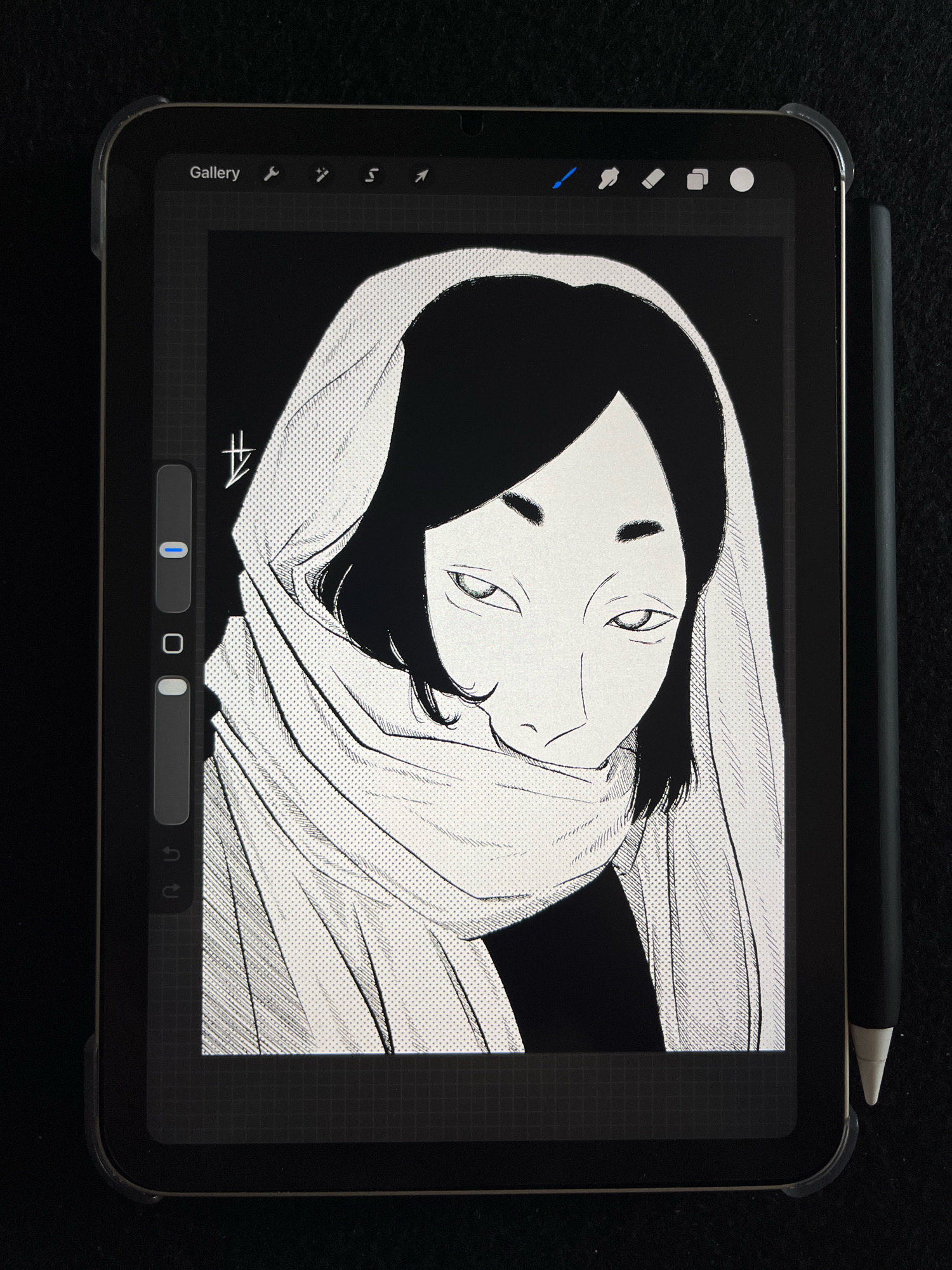 The image is a close-up shot of a tablet displaying a black and white digital drawing of a person wearing a headscarf or hood. The artwork features detailed linework and dot shading. The tablet is placed on a dark, textured surface, possibly a desk or cloth. A stylus pen, likely for the tablet, is positioned to the right of the device. The tablet's user interface is partially visible at the top, showing icons like "Gallery," a brush, and other tools. The drawing itself is the primary focus, with the subject's face looking towards the viewer with a somewhat intense gaze, partially obscured by the fabric. The overall composition is stark due to the high contrast of the drawing and the dark background. There is no indication of the city of Wałcz, Poland, in the image.