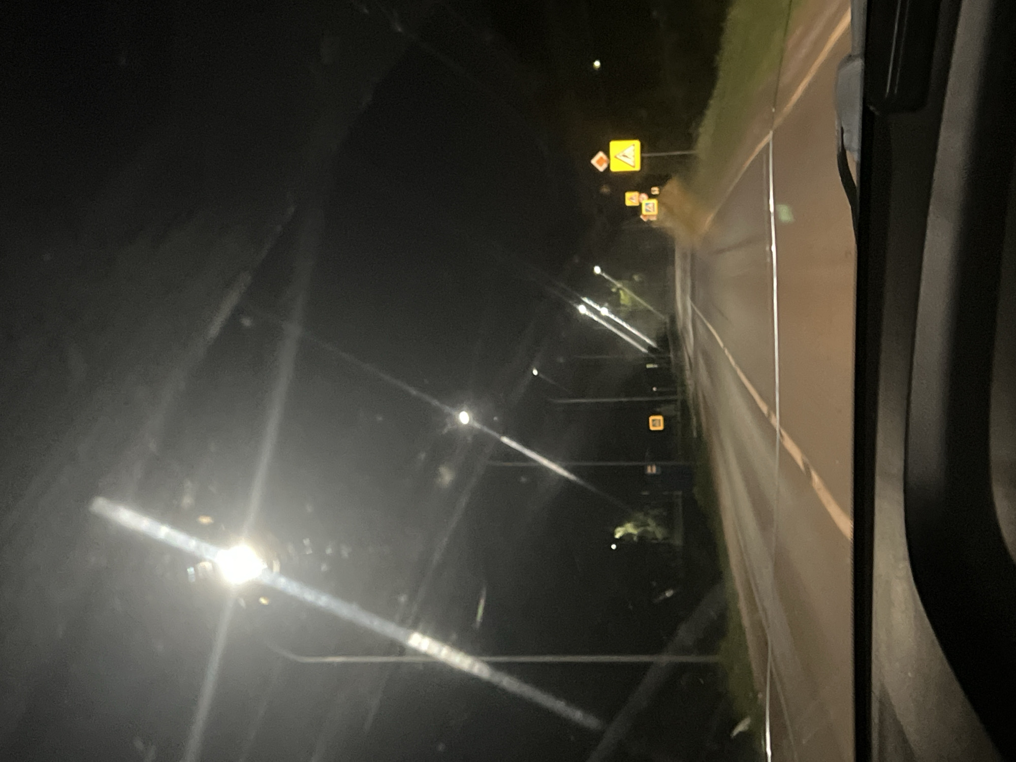 A night view from a vehicle, presumably a truck, traveling on a road. Street lights are visible along the roadside, as well as road signs. The location is likely near the city of Бизяки, Russia, as indicated by the Russian road signs. The road appears wet.