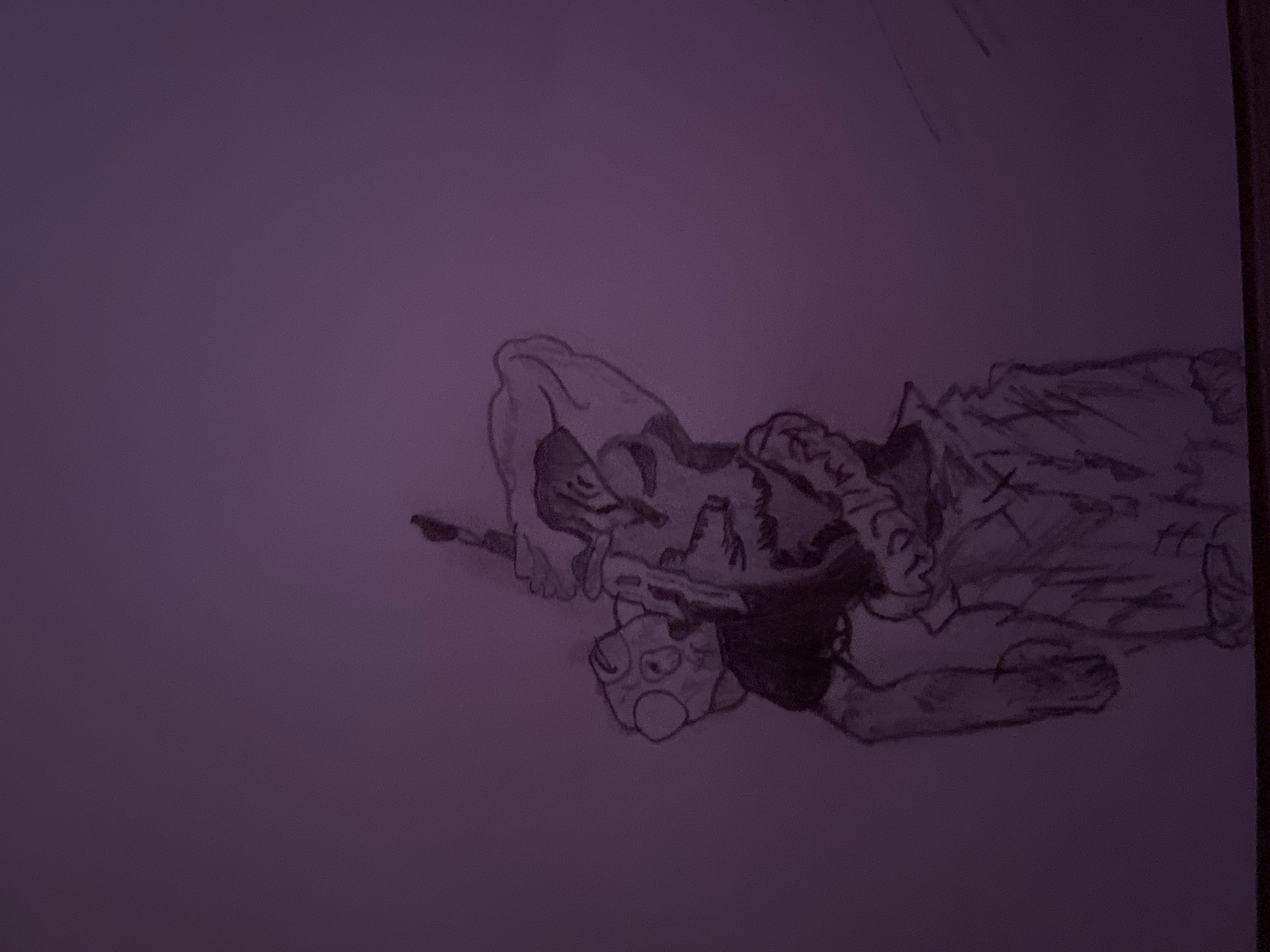 The image depicts a hand-drawn sketch of a person or character lying on a surface. The figure has detailed facial features, possibly intended to appear grotesque or monstrous. The figure is wearing clothing, including what appears to be a shirt or jacket with detailing. A small object rests near the figure's head, possibly a toy or doll. The sketch is on a piece of paper against a plain purple background. There is no information in the image that would indicate a location in Zlatograd, Bulgaria.