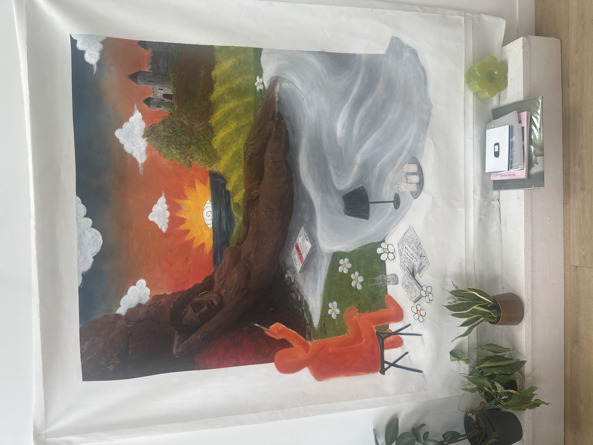 The image presents a painting attached to a white wall. The painting appears to depict a juxtaposition of contrasting scenes. On the left side, there's a landscape with a sunset, clouds, a castle in the distance, and a figure reclining on a rock formation. The right side shows a lighter scene with a grey-scale depiction of what seems to be a room setting including a table, a lamp, candles, a painting, and white flowers scattered in a grassy area with an orange figure seated in a chair with a paintbrush or other writing utensil in hand. The painting's subject matter and style have a surreal quality.
The setting seems to be an indoor space, evidenced by the white walls and the presence of decorative items such as a green flower-shaped object, a stack of books or papers, and several potted plants (including a snake plant) on a tiered shelf next to the painting. The environment lacks specific details that would definitively place it in Saint-Denis, France, but the subject of the painting might be inspired by the city.