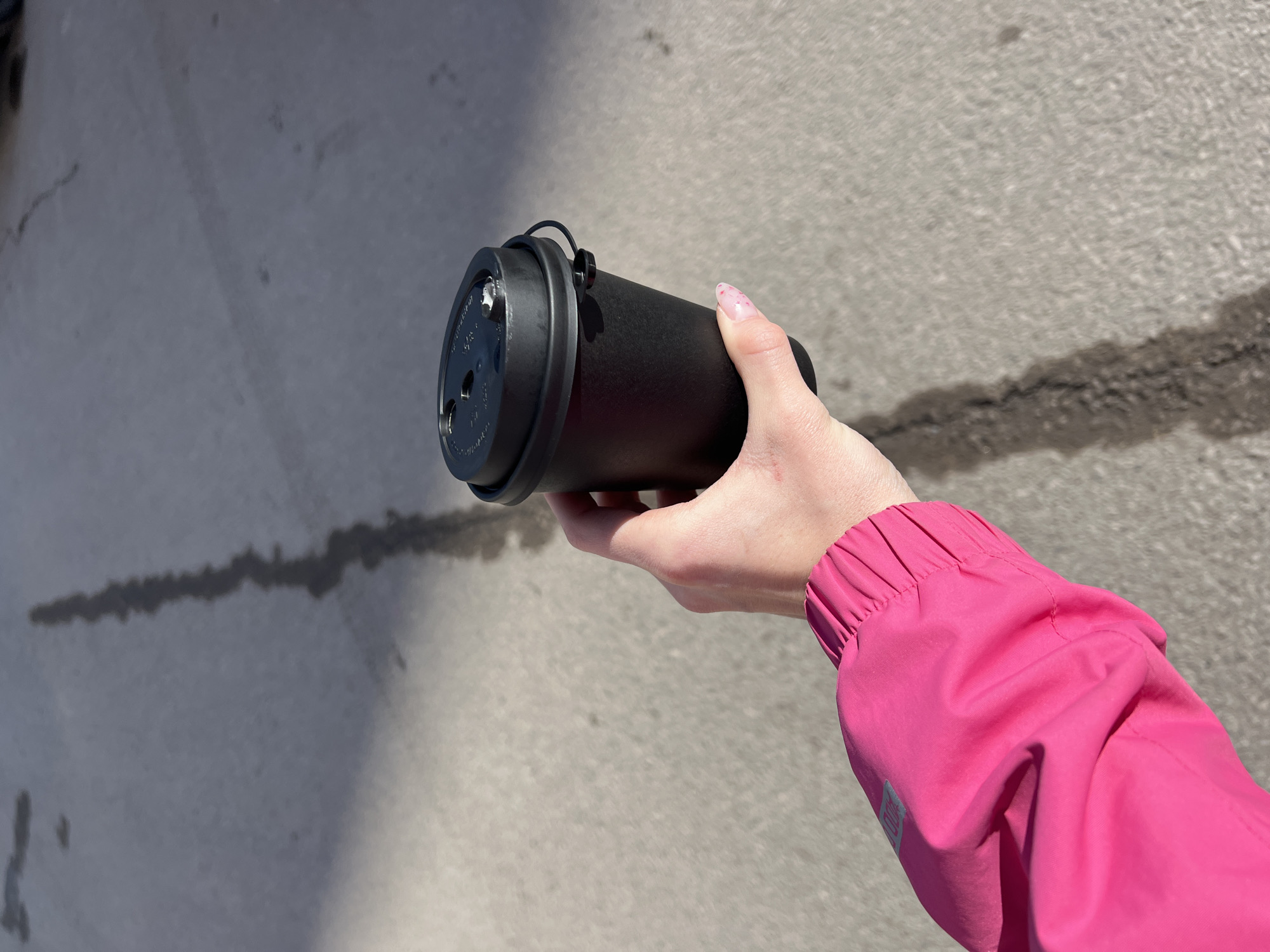 A person wearing a pink jacket is holding a black thermos in their right hand. The location appears to be outdoors on a concrete surface with a dark, irregular stain running across it. Berezniki, Russia cannot be verified from the visual information provided.