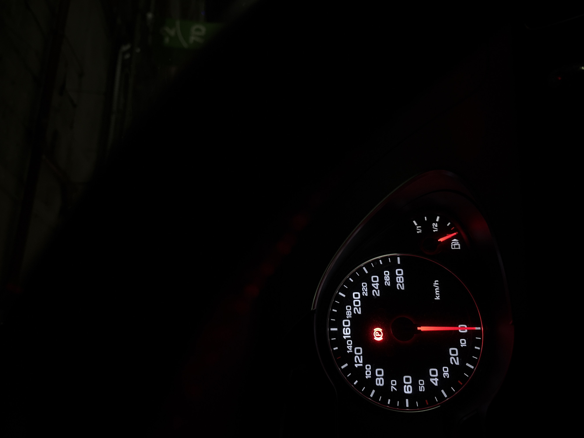 A close-up, low-angle shot depicts the illuminated speedometer of a vehicle, showing a speed of approximately 3 km/h, with the parking brake light illuminated, and the fuel gauge reading slightly below full. The vehicle seems to be stationary. The background is predominantly black, suggesting nighttime. The presence of a sign with "7D" visible in the upper-left corner indicates the vehicle is likely in a location in Sofia, Bulgaria, where 7D route buses are common. The environment is very dark and only the dashboard is fully visible.