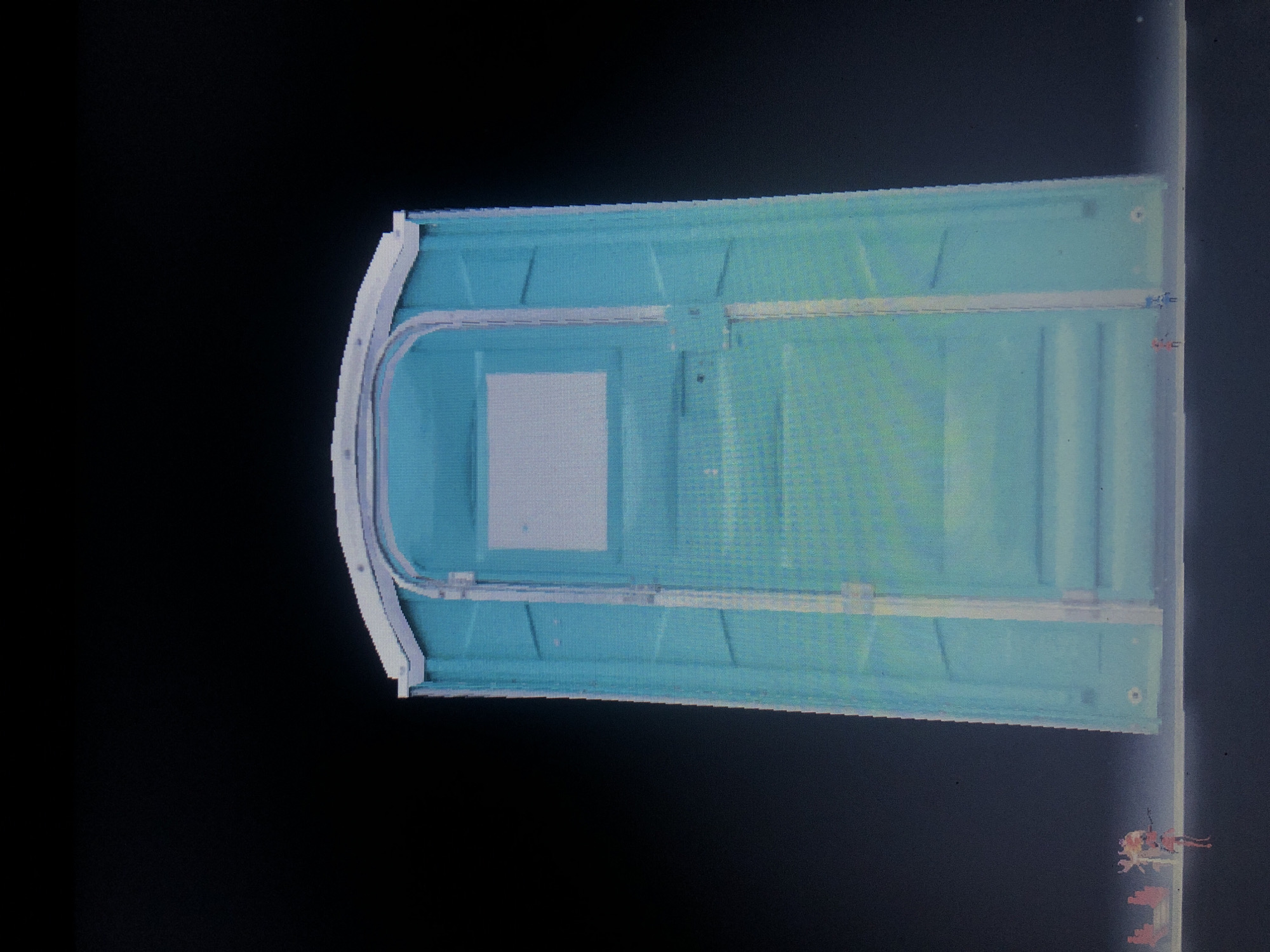The image depicts a portable toilet, possibly a single unit restroom, against a black background. It is light blue with a white, rounded corner section and a rectangular window. The scene provides no context for determining the location in Buenos Aires, Argentina, or identifying any subjects, actions, or interactions. The description is limited to the object itself.