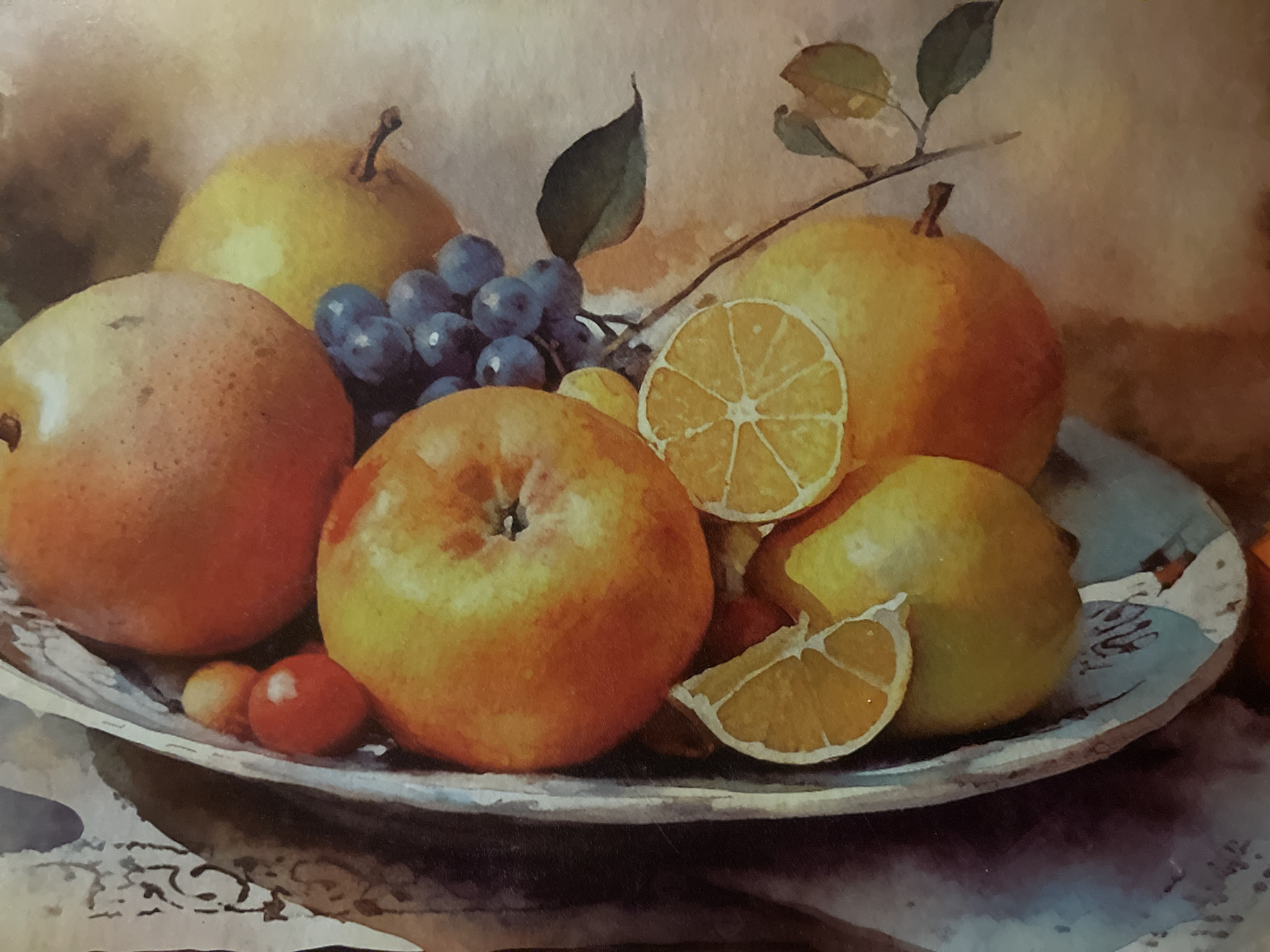 The image is a watercolor painting depicting a still life of fruits in a bowl. The bowl is elongated and appears to be made of ceramic, with a decorative rim. Inside the bowl, various fruits are arranged: several apples, grapes, pears, and slices of citrus fruit, possibly oranges or lemons. The colors are rich and vibrant, with warm tones dominating the palette. The background is softly blurred, suggesting a textured surface or fabric. There is no indication of any specific location within the city of Minsk, Belarus, or any people or actions. The focus is entirely on the artistic rendering of the fruit composition.