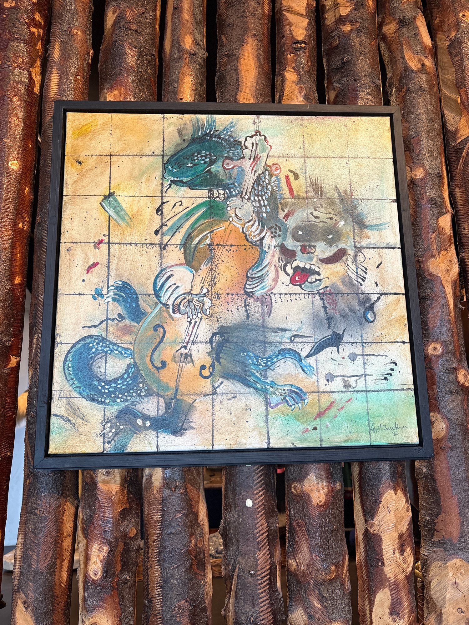 The image shows a framed painting with a dark frame, mounted on a rustic background of vertical, rough-hewn wooden logs. The painting itself is square and appears to be an abstract or surreal depiction of a creature playing a cello. The creature is predominantly green and blue, with sharp spiky features and a long, serpentine body. It has skeletal-like hands holding a bow and fingers on the fingerboard of the cello, which is also rendered in abstract, earthy tones of orange and brown. The background of the painting is a grid-like pattern with splatters of red and black paint, suggesting a chaotic or energetic composition. A face with a wide, open mouth and protruding tongue is visible in the upper right quadrant of the painting. The artist's signature, "Krist Beedham '91", is visible in the lower right corner of the painting. The overall setting, with the rough logs, suggests an outdoor or rustic environment. No specific location in Reykjavik, Iceland, can be determined from the image alone.