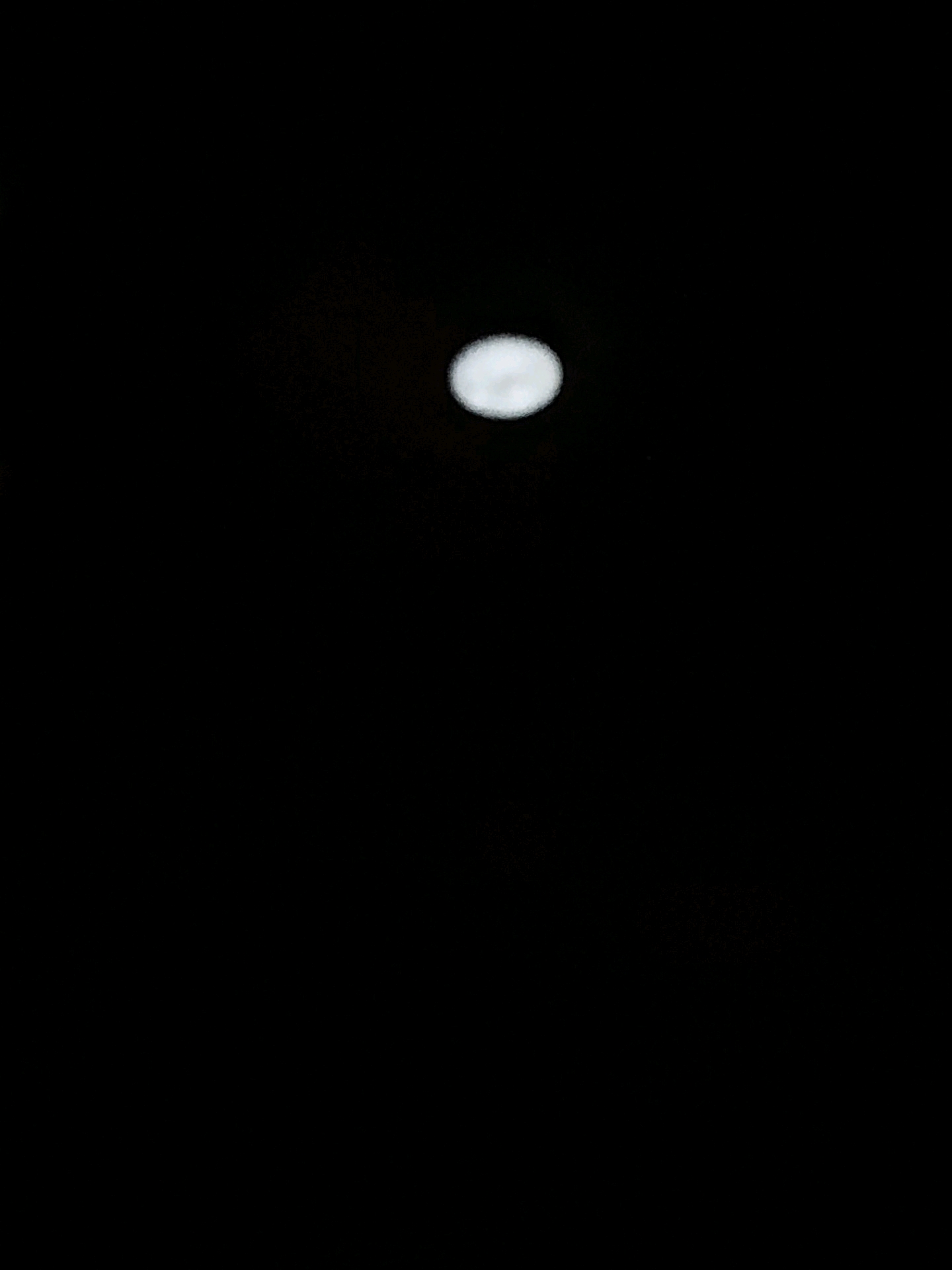 A slightly out-of-focus, bright circular object, likely the moon, is visible against a dark, black background, suggesting it is nighttime. The object is located towards the top center of the image. There are no discernible urban features or landmarks present to indicate a specific location within Mumbai, India. The scene is devoid of any people, objects, or actions.
