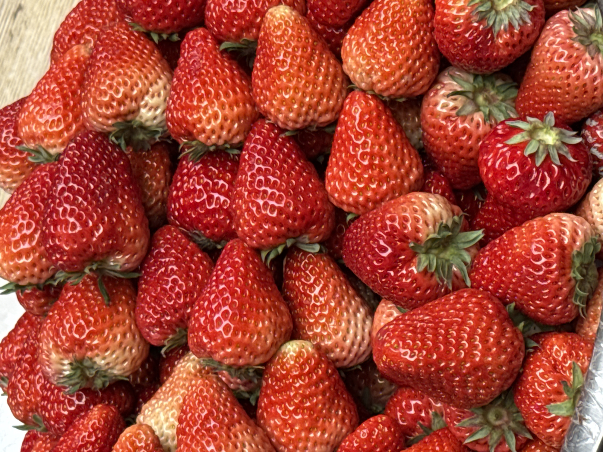 A close-up shot displays a large pile of fresh, red strawberries with green stems. The strawberries are various sizes and shapes, appearing ripe. The background is a light-colored surface. There's no evidence suggesting this scene is specifically in Jinjiang District, China. The information about the location can't be confirmed based on the visual content alone.