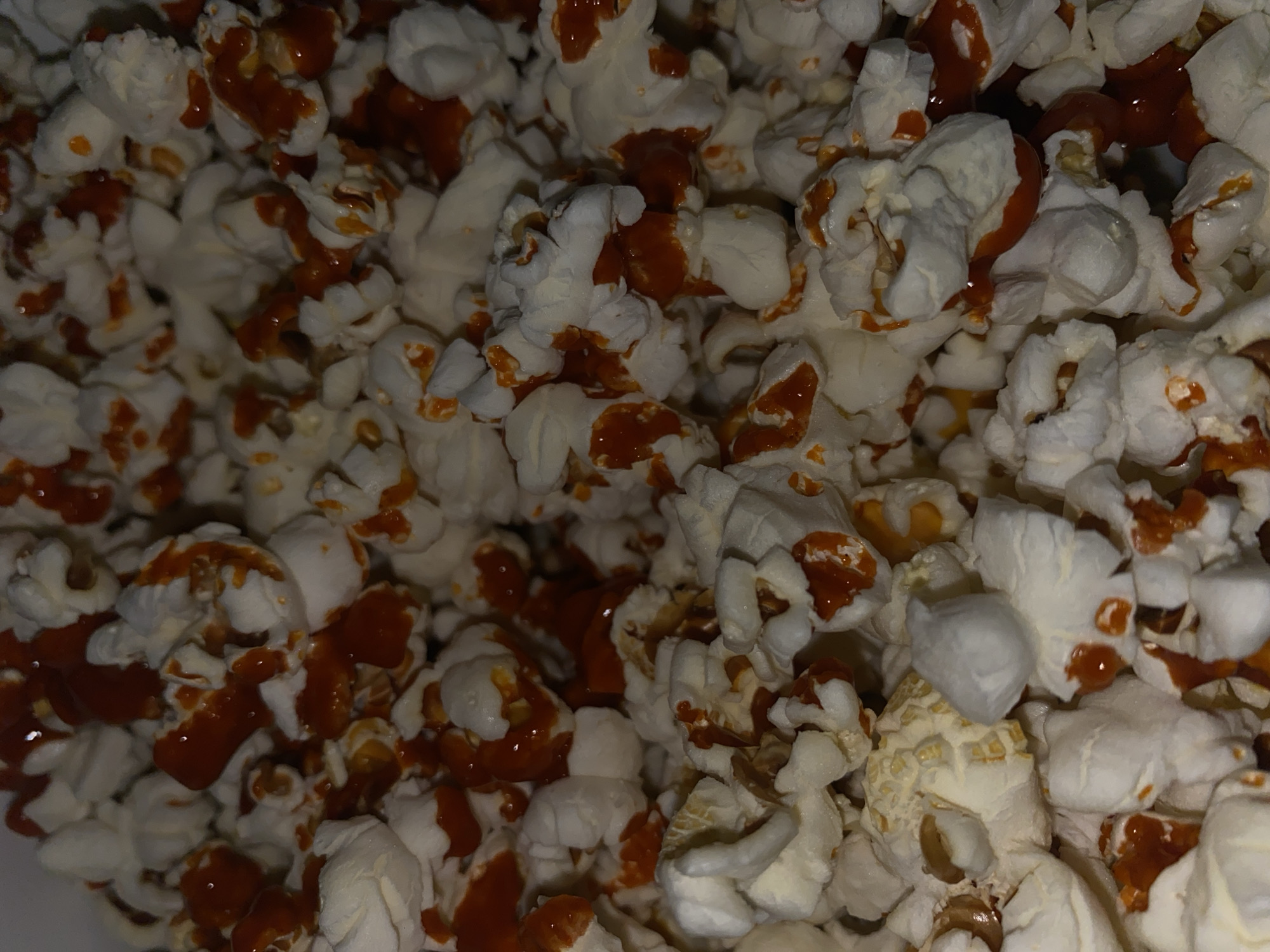 The image shows a close-up view of caramel popcorn. The popcorn pieces are mostly white with drizzles of caramel sauce.