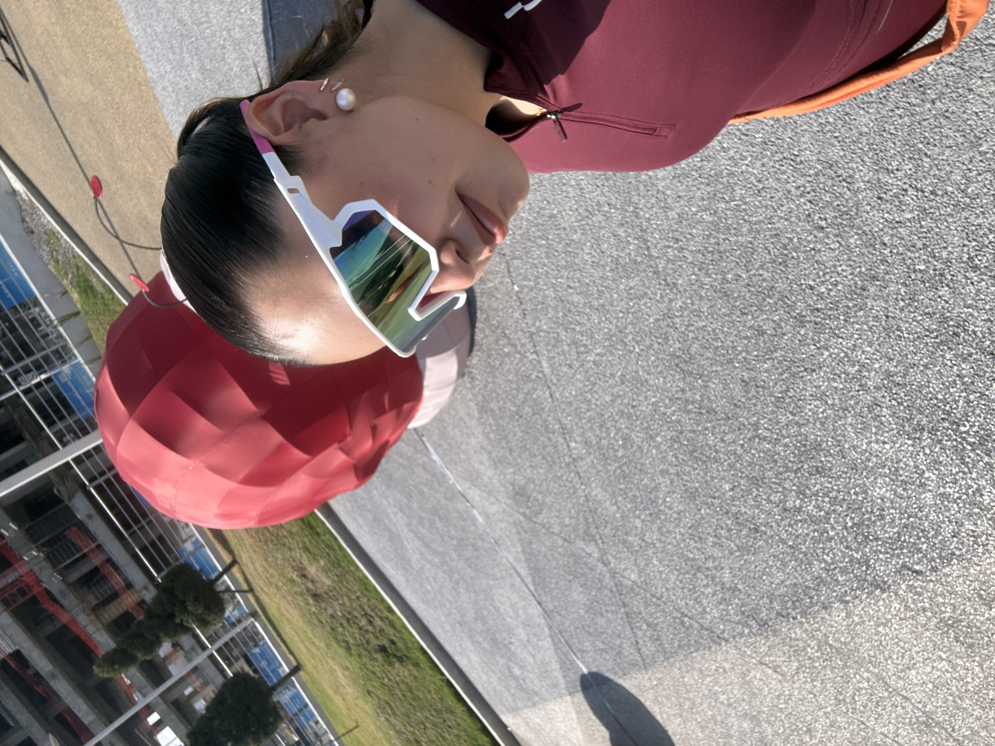 The image shows a woman wearing sunglasses and a burgundy top. A large red balloon is nearby. In the background, there's a view of a construction site, trees, and a grassy area. Based on this information, the location appears to be an outdoor setting in Puebla, Mexico.