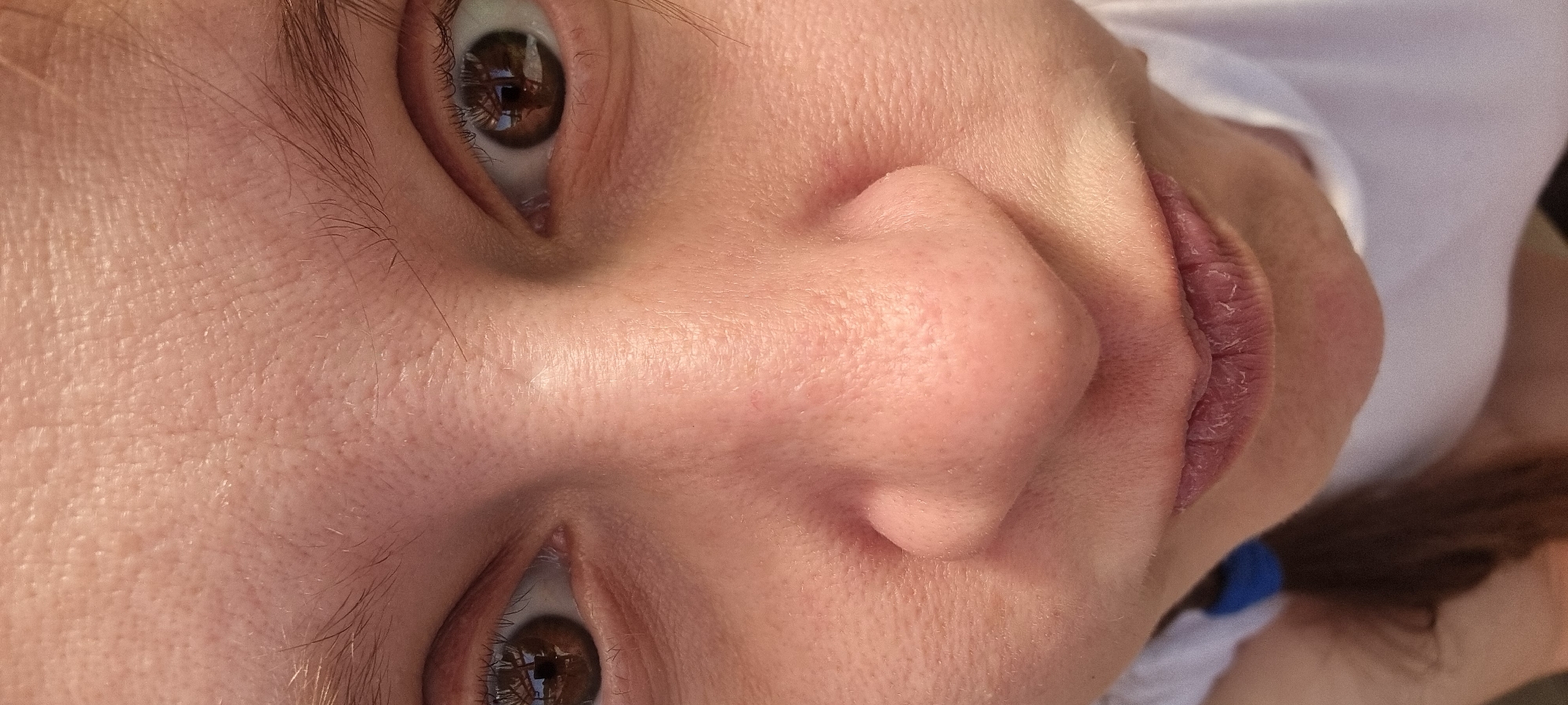 A close-up, angled view of a person's face. The focus is on the facial features, including the eyes, nose, and lips. The person has brown eyes, and their skin appears smooth. The lips are slightly dry. The angle suggests the person might be lying down. There are reflections in the eyes. The environment is undiscernible, and there's no verifiable connection to Dunnae-myeon, South Korea.