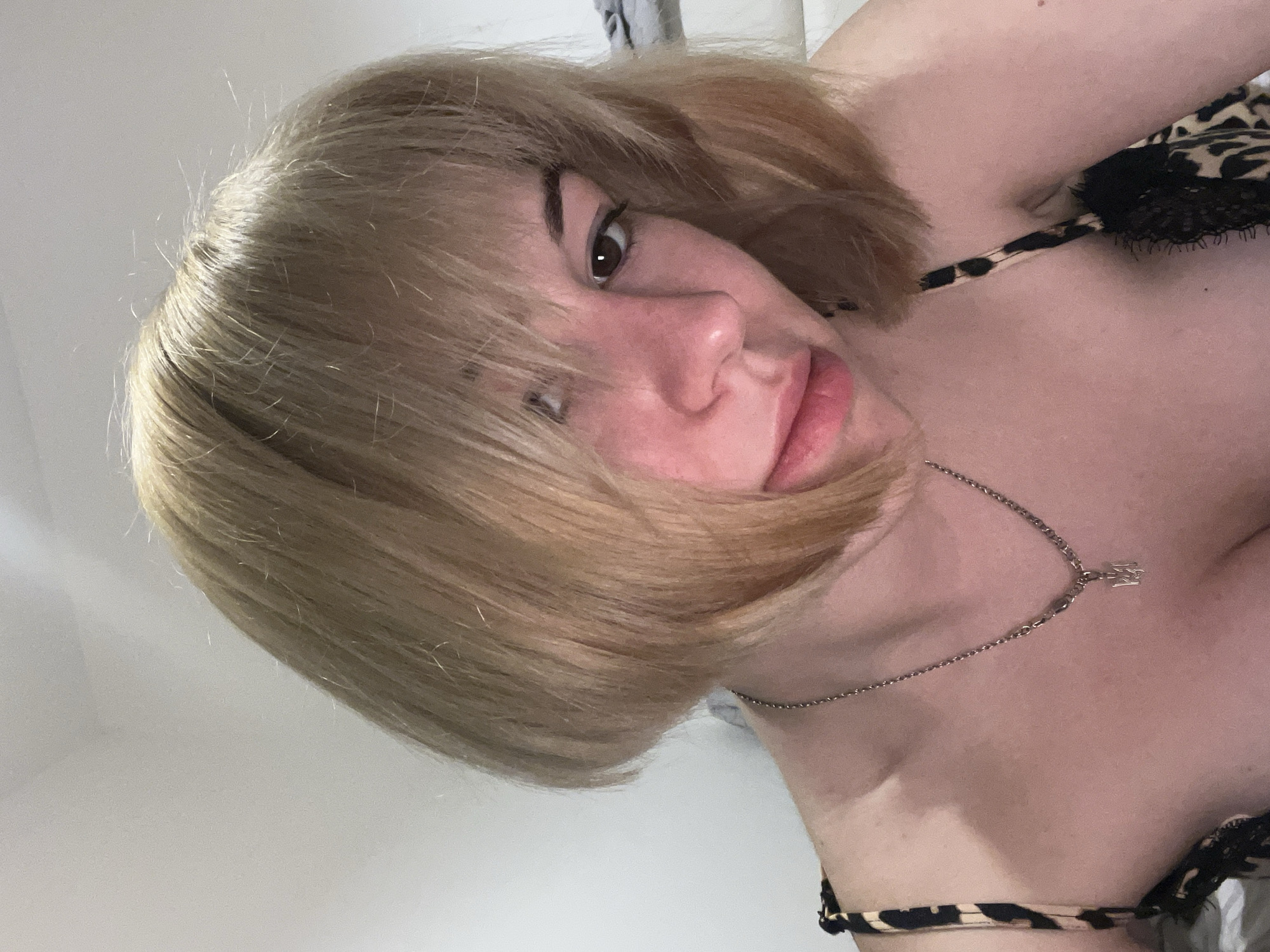 A close-up, slightly rotated image features a woman with short, light blonde hair and brown eyes. She is wearing a necklace with a pendant. The woman is wearing a leopard print top with black lace details. The background is a plain, light-colored wall. The location is unspecified and there is no evidence of Boreti, Montenegro.
