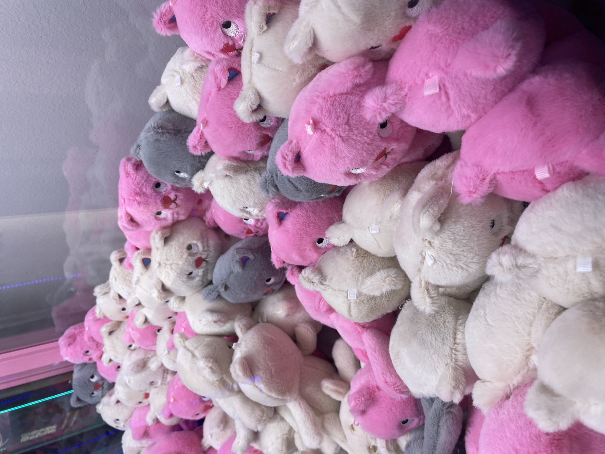 A pile of plush toys, predominantly pink and white with some grey, fills a claw machine. The toys are in various states of disarray, some upright and others lying on their sides. The lighting suggests an indoor environment, likely a commercial space. There are no people visible in the image. The location in Vaganovo, Russia, is not visually evident from the image.