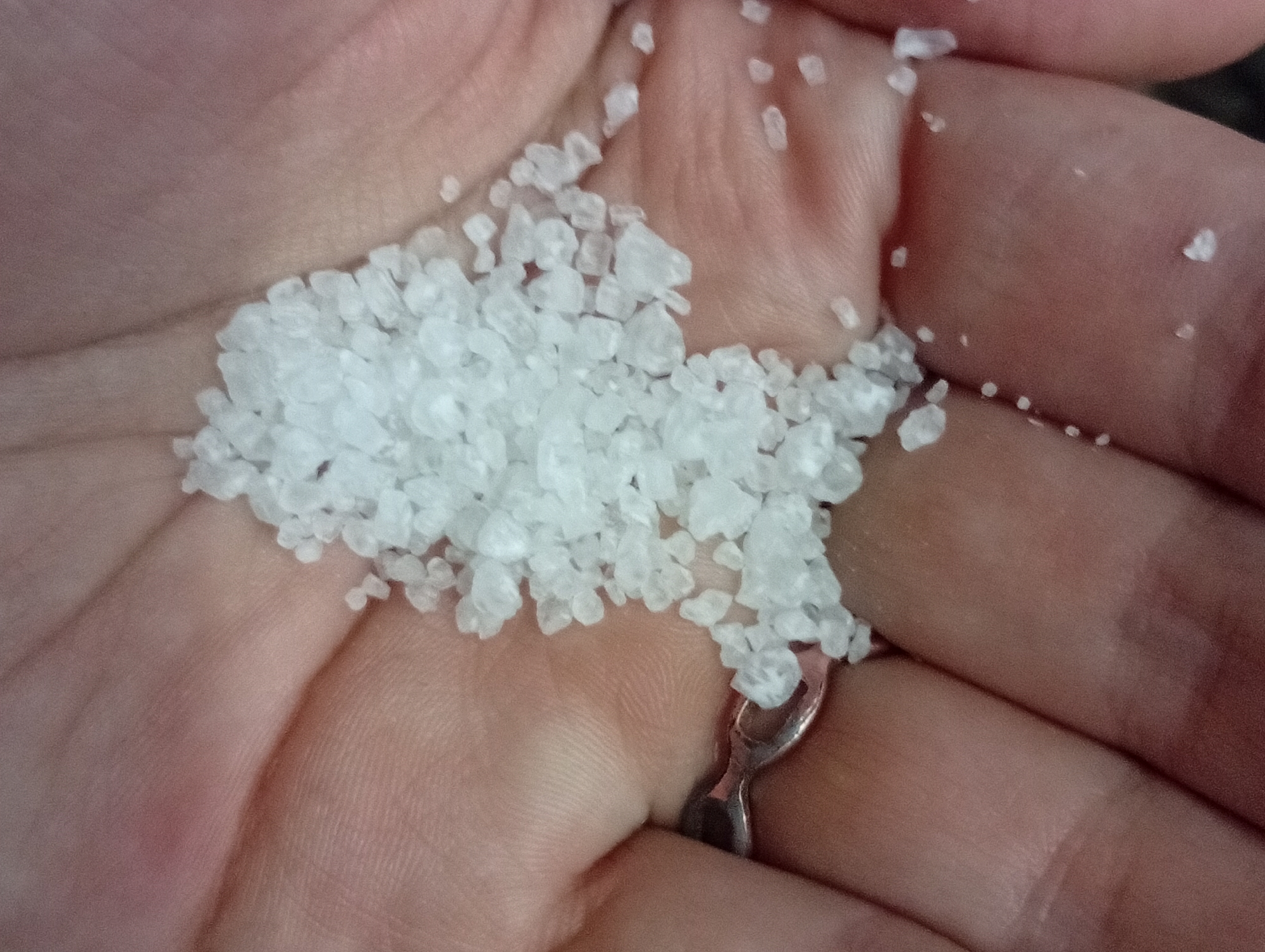 A close-up photograph depicts a human hand holding a quantity of white, crystalline material. The material appears to be coarse salt or a similar substance. A simple metal ring is visible on one of the fingers. The skin of the hand is pinkish, and the background is blurred. There is no visible information to determine the location of this scene in the city of Buenos Aires, Argentina.