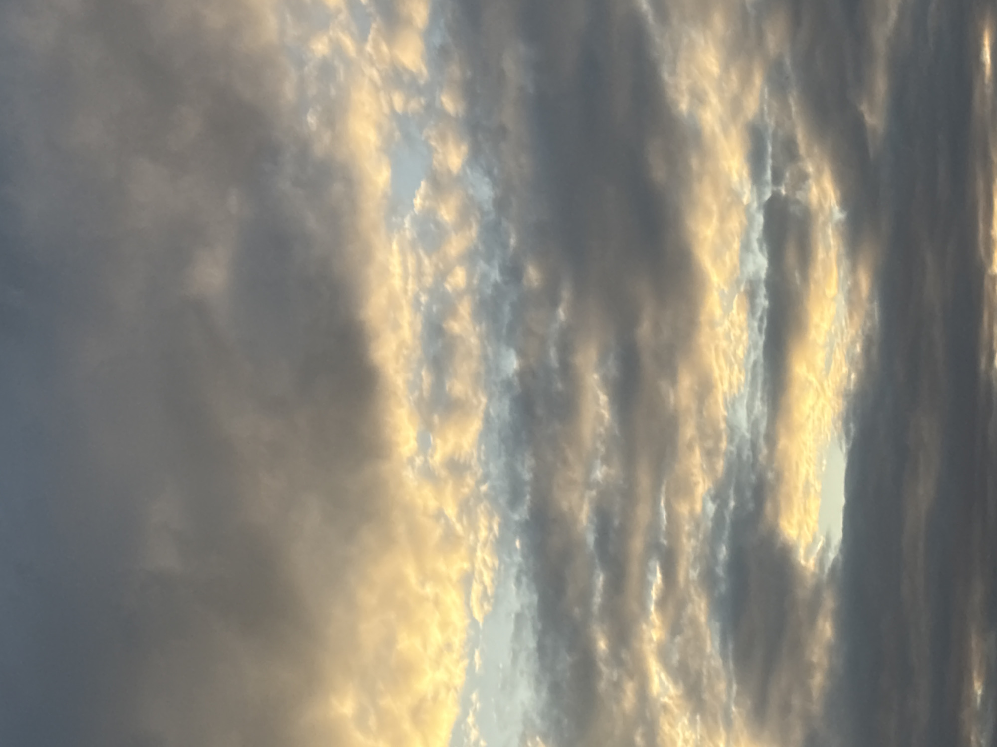 The image shows a dramatic sky filled with clouds at sunset or sunrise. The clouds are a mix of dark grays and lighter, golden-yellow hues, suggesting the sun's rays are breaking through or reflecting off them. There are also patches of bright blue sky visible between the clouds. The scene is devoid of any structures, people, or identifiable landmarks that would indicate a specific location within Georgiyevsk, Russia, or any other city. The focus is solely on the atmospheric conditions.