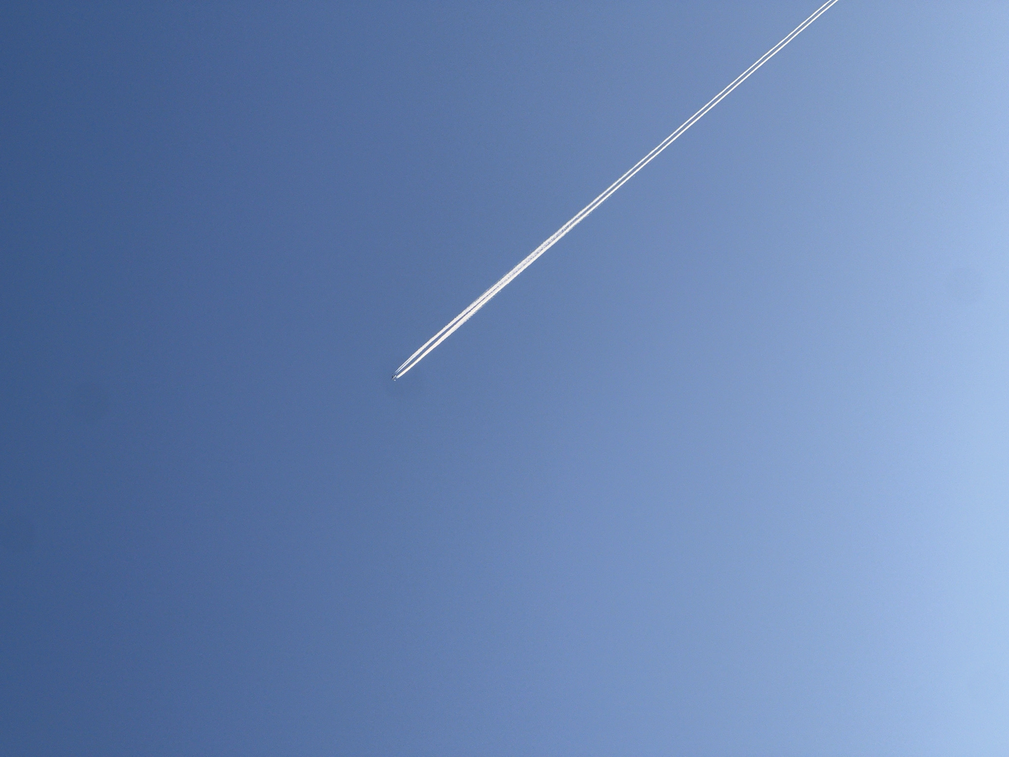 A jet airplane flies through a clear, blue sky, leaving a white contrail behind it. The location is not specified, and there is no indication that the image was taken in Budva, Montenegro.