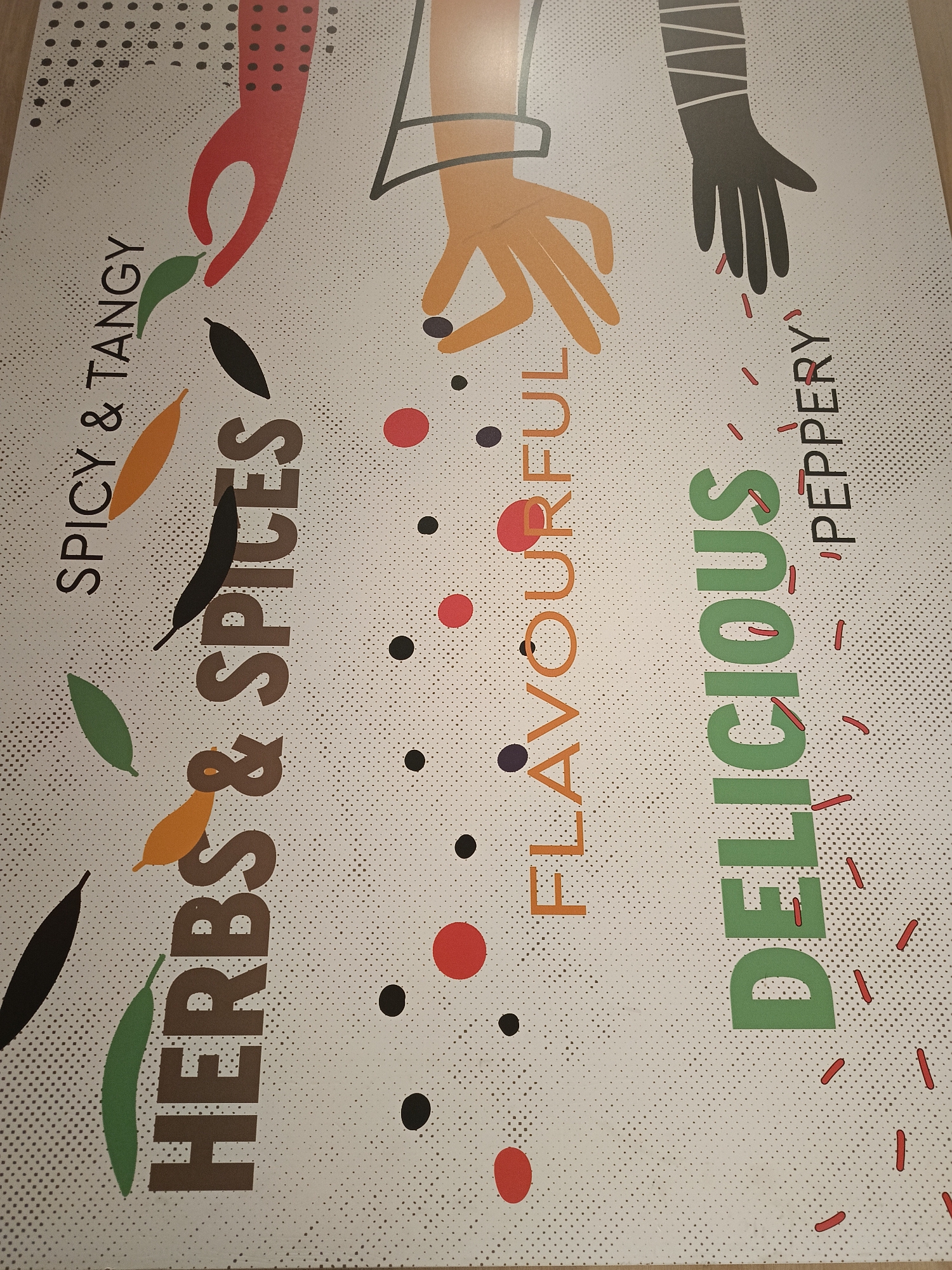 The image is a close-up of a promotional graphic with the phrases "SPICY & TANGY," "HERBS & SPICES," "FLAVOURFUL," and "DELICIOUS 'PEPPERY'" displayed alongside stylized illustrations of hands and various spices. The background is a white surface with a dotted pattern. A red hand is at the top left, an orange hand is at the top center, and a black hand is at the top right. Red, black, and brown dots are sprinkled throughout the graphic. The image does not depict any identifiable location in Izhevsk, Russia, or provide any forensic details related to a scene.