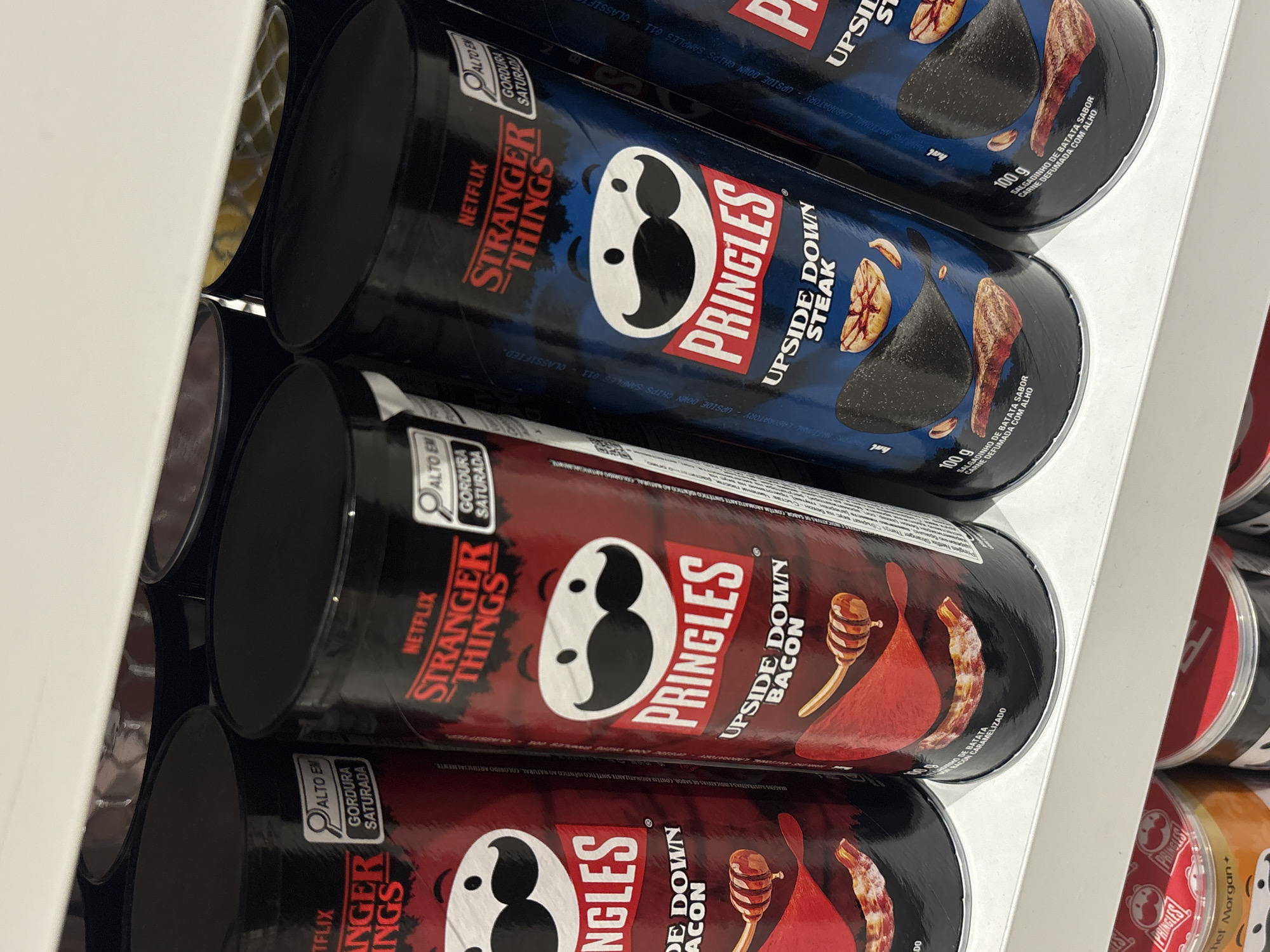 The image shows a close-up of a shelf stocked with Pringles potato chip cans. Two varieties are visible: "Upside Down Bacon" (red packaging) and "Upside Down Steak" (blue packaging), both displaying a "Stranger Things" Netflix branding. The cans are stacked vertically, partially obscuring others. A white shelf is visible on the left and right edges. The image does not provide any information about the city of Varna, Bulgaria, nor any indications it was taken there.