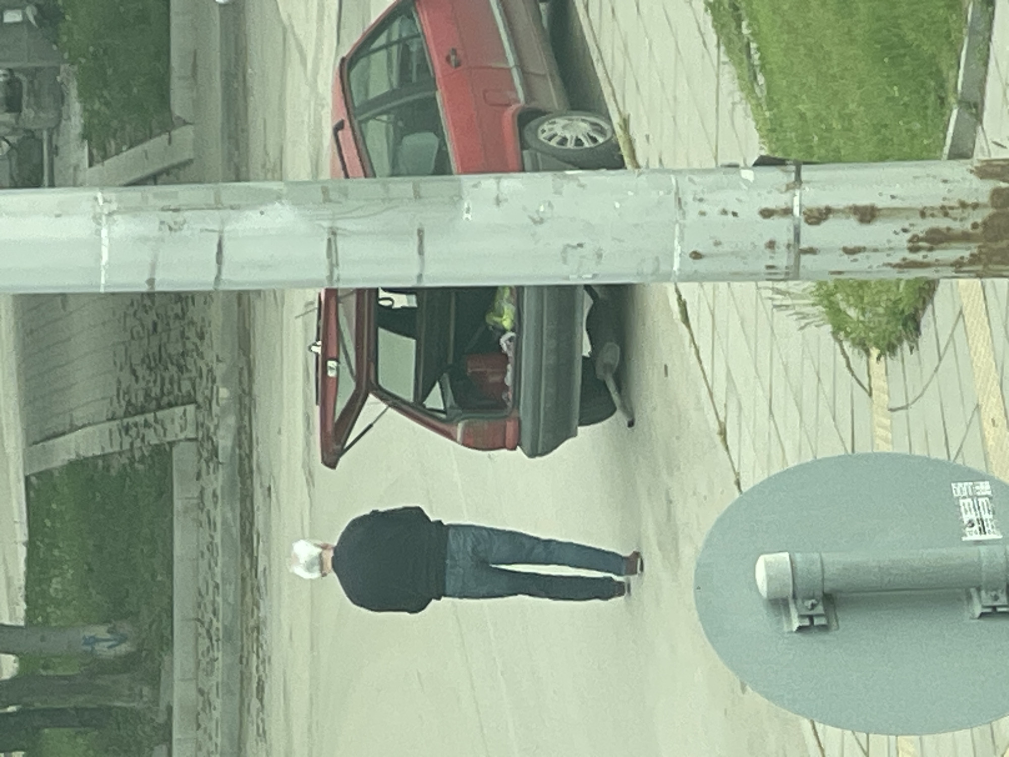 A person is standing next to a red car on a street in Sofia, Bulgaria. The car's trunk is open. A sign is visible on a post, and trees and grass are on the side of the street.