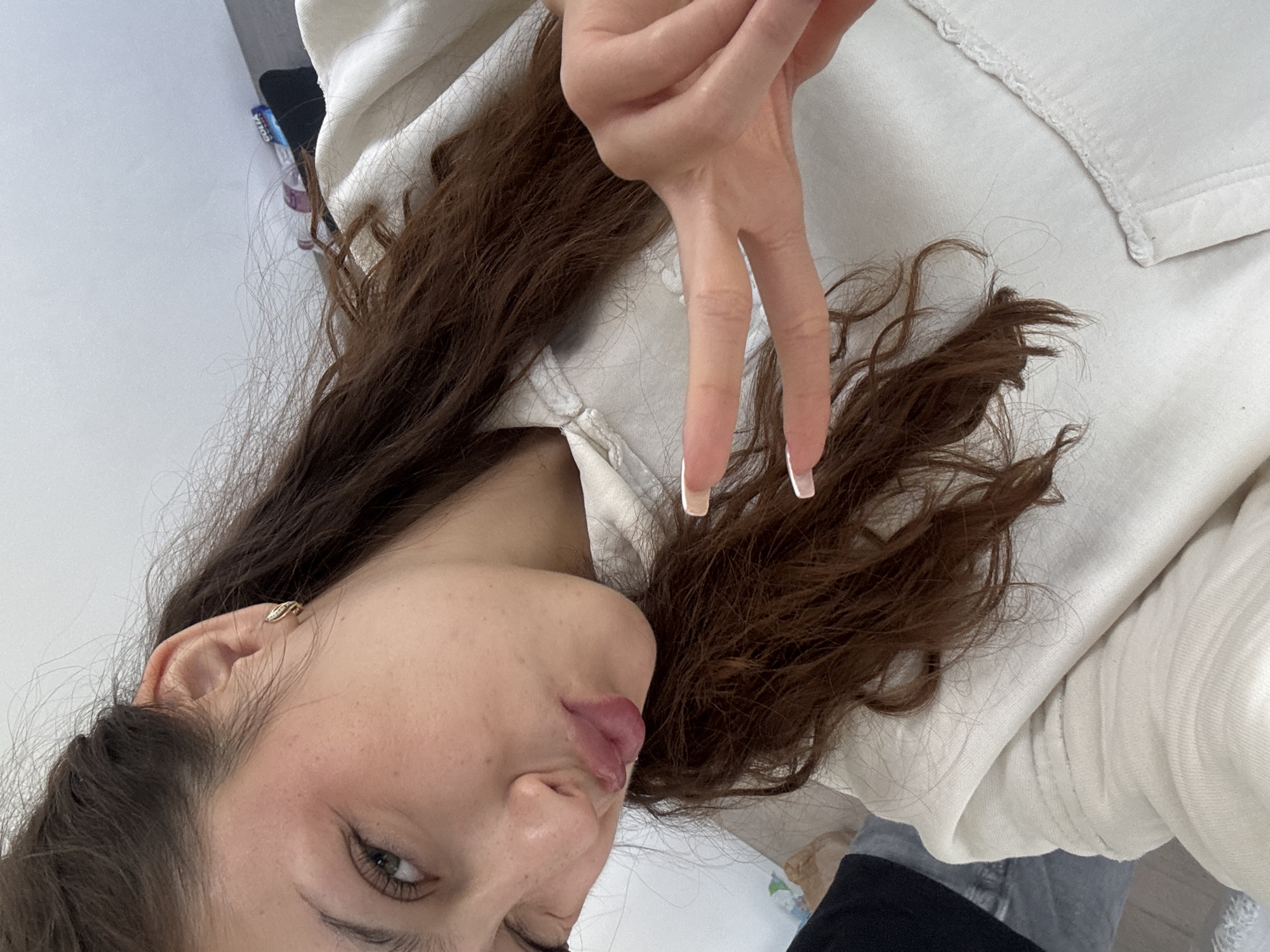A woman poses for a selfie, holding up a peace sign with manicured nails. She has brown hair and is wearing a light-colored shirt. The photo appears to have been taken indoors, but there is no indication in the image that would relate to the city of Milan, Italy. Therefore, there is no forensic information in the image to support the location.