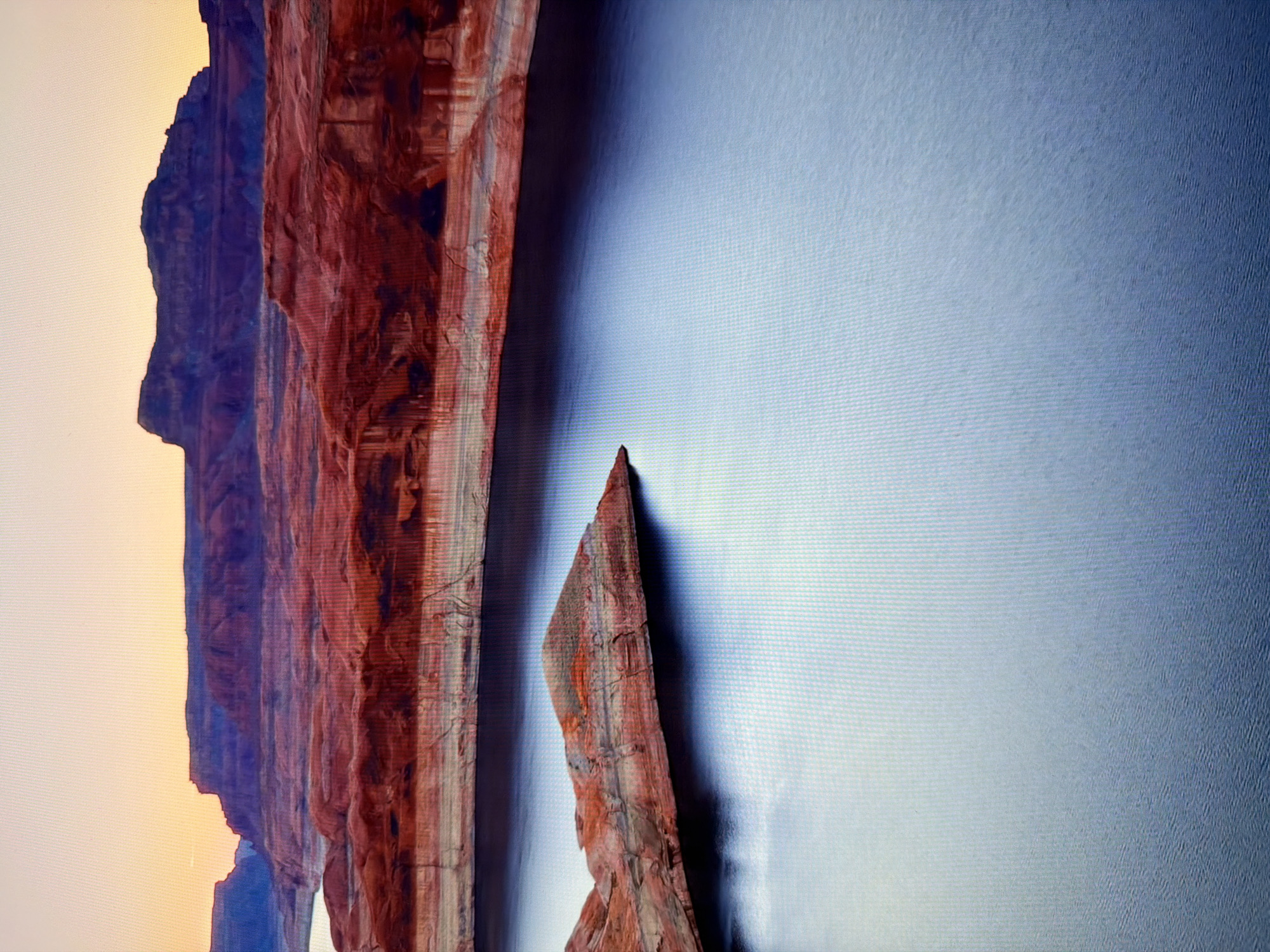The image shows a wide, still body of water, likely a lake, with red-toned rock formations along its edges. The formations exhibit distinct horizontal layering, characteristic of sedimentary rock. The water reflects the soft, warm hues of a sunset or sunrise, with the sky transitioning from a pale yellow to a soft orange and then a deep purple at the horizon. In the foreground, a small, triangular rock island juts out from the water. The overall scene evokes a sense of natural grandeur and tranquility. The image does not contain any elements that would indicate a location in Kyiv, Ukraine; it depicts a natural landscape.