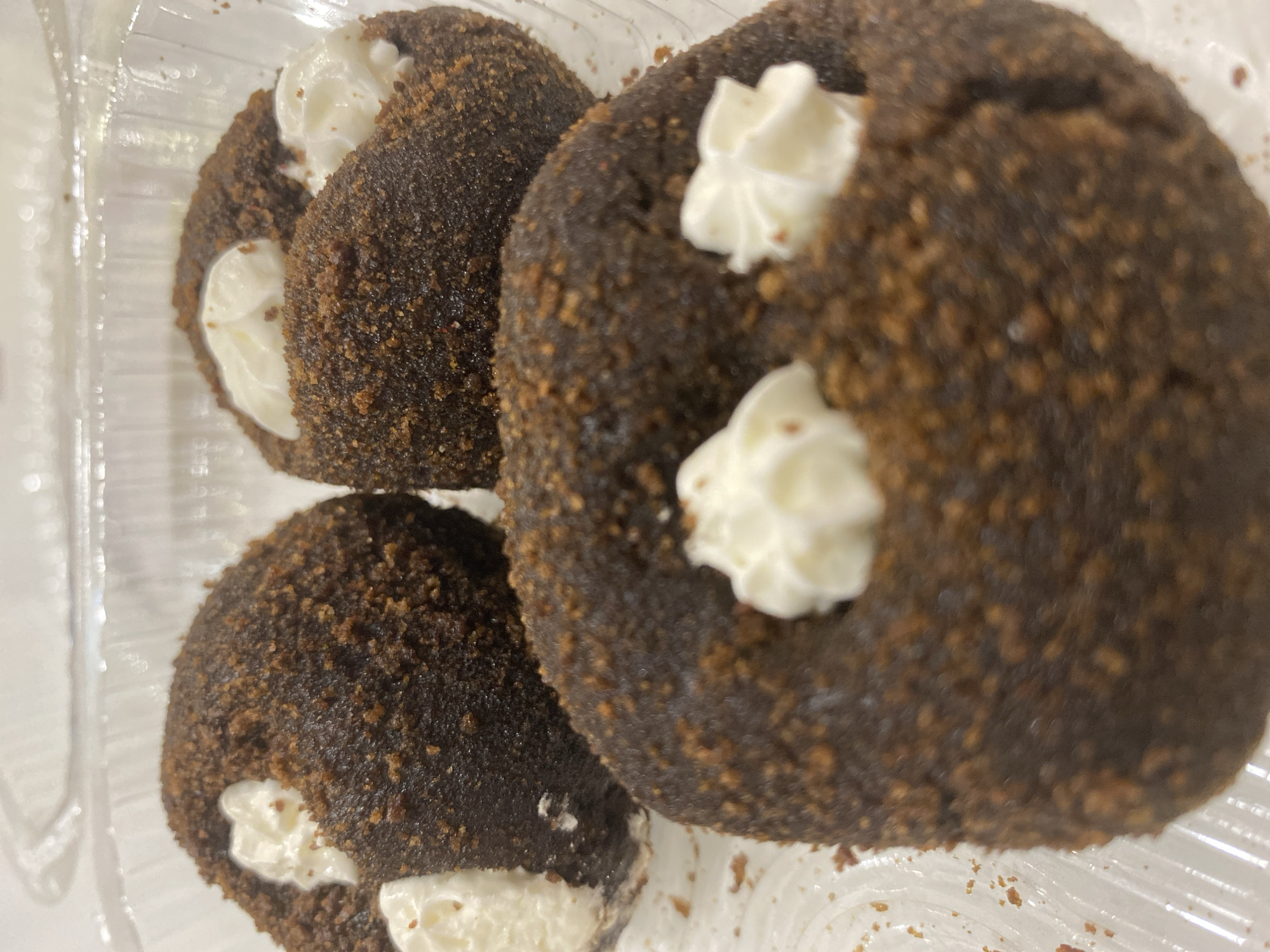 The image shows three chocolate-covered pastries filled with white cream. The pastries are round and have a crumbly texture on the outside, with dollops of cream on top. They are arranged in a clear plastic container. The context provided, that this image is in Tyumen, Russia, cannot be visually verified from the image itself.