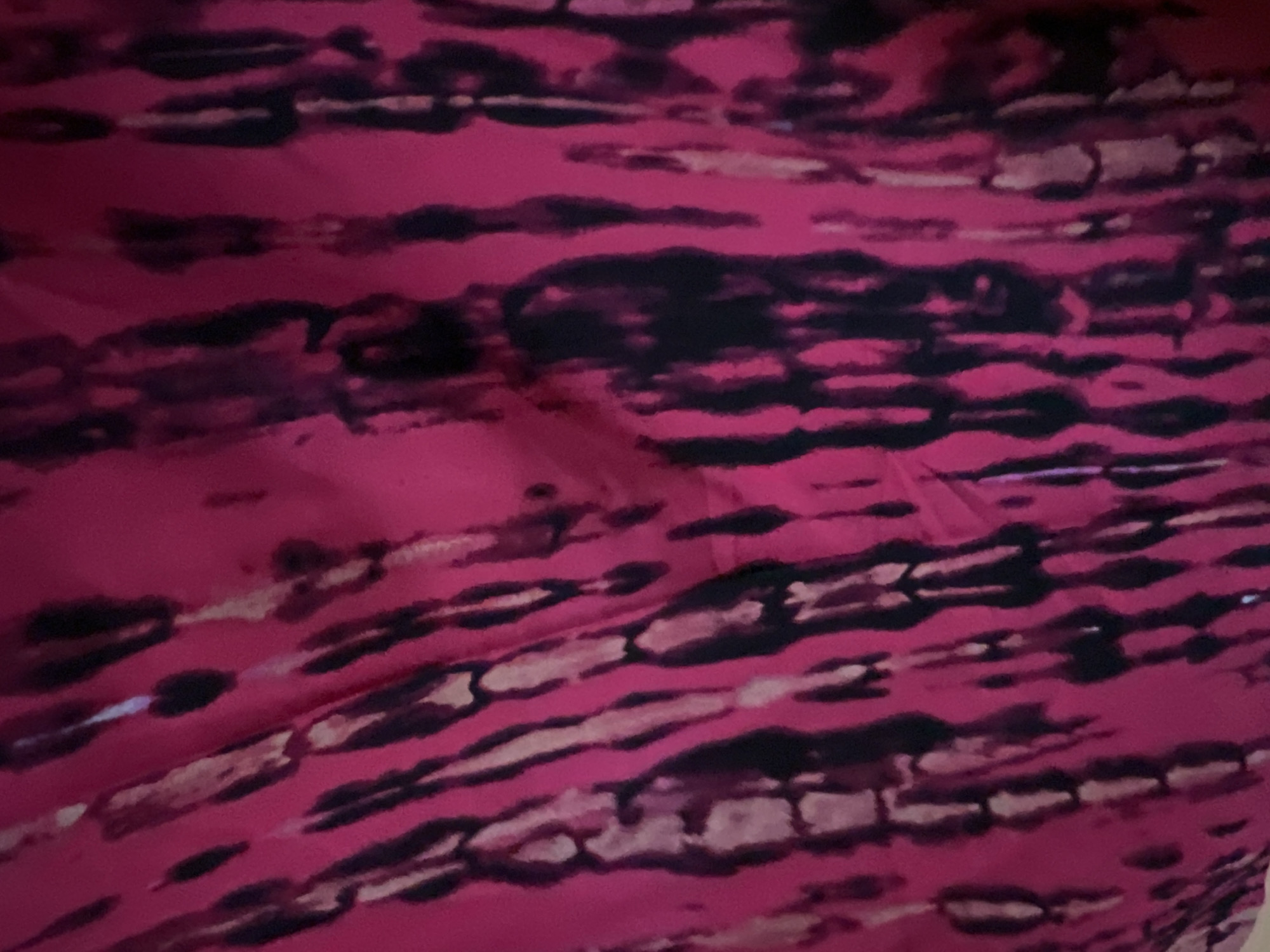 The image shows a close-up, abstract view of a pink fabric with a tie-dye pattern of black and white streaks. The fabric appears to be draped or folded, creating subtle shadows and highlights that enhance the texture of the material. There are no discernible features of the city of Minsk, Belarus, or any people, subjects, objects, or actions that would indicate a specific location or context.