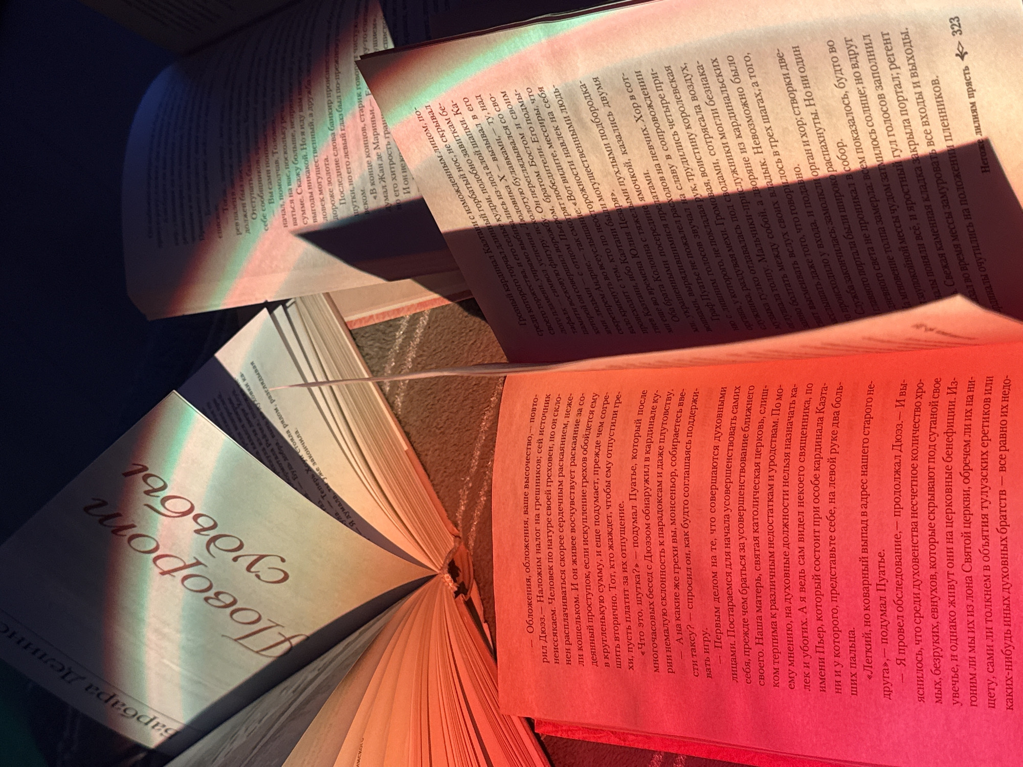 Here is a description of the image:
The photograph shows a book open with its pages spread out, along with other books in the background. The opened book has Russian text visible on its pages, with "Поворот судьбы" (Turn of Fate) prominently displayed. The image is brightly lit with colorful light, casting a red glow on the lower pages and a blue-green hue on the upper pages. The background contains partially visible pages of other books, also with Russian text. The overall composition creates a sense of depth and literary exploration.