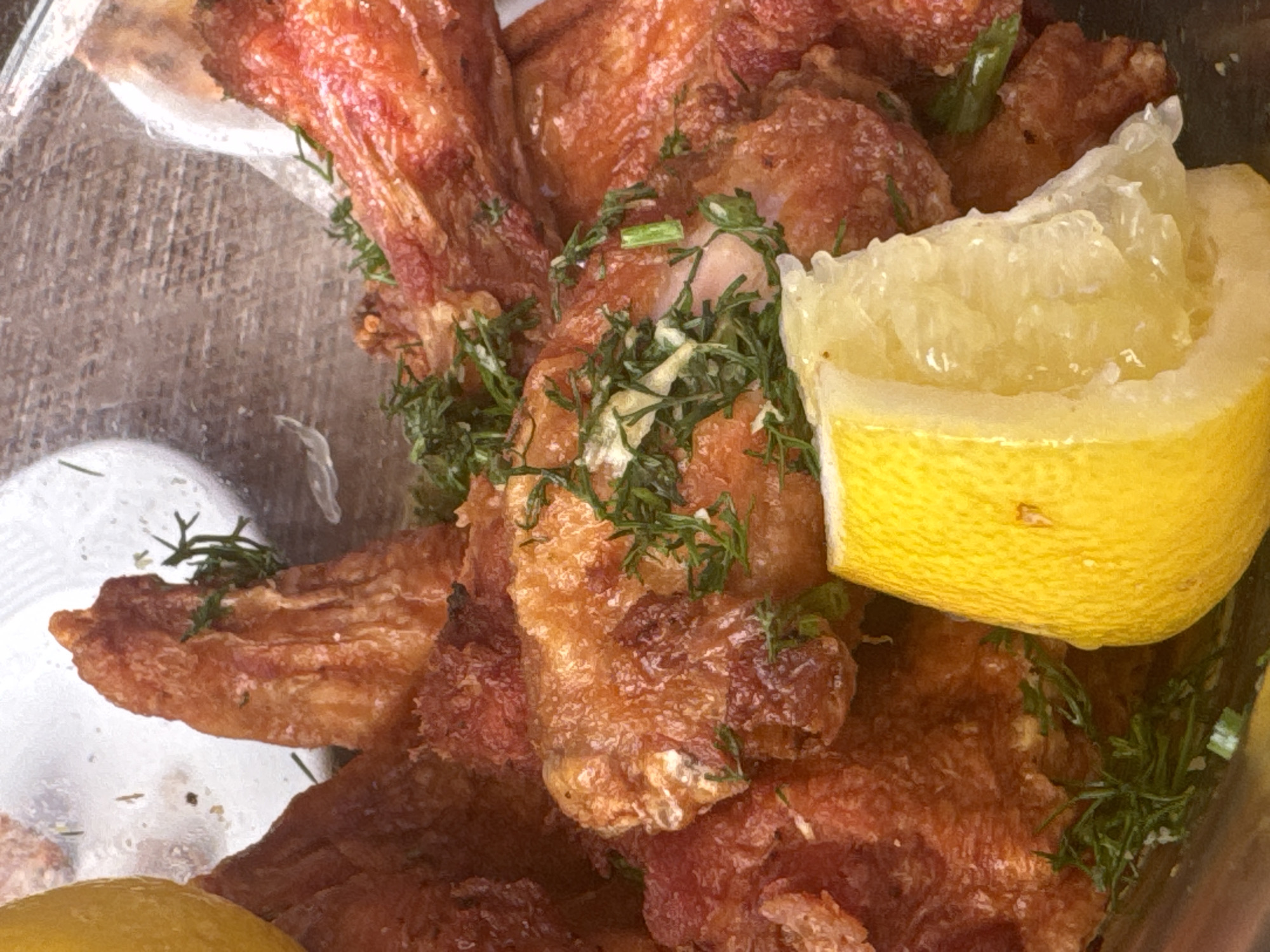 The image depicts fried fish fillets garnished with chopped dill and lemon wedges, likely in a plastic takeout container. The origin location cannot be verified.