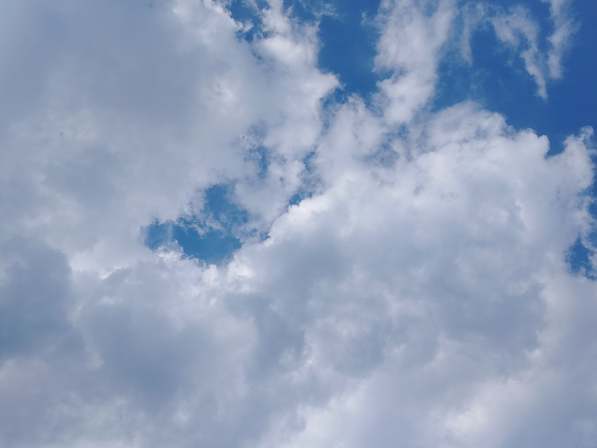 The image shows a sky with white and grey clouds. Some patches of blue sky are visible between the clouds. The location and city are unknown.