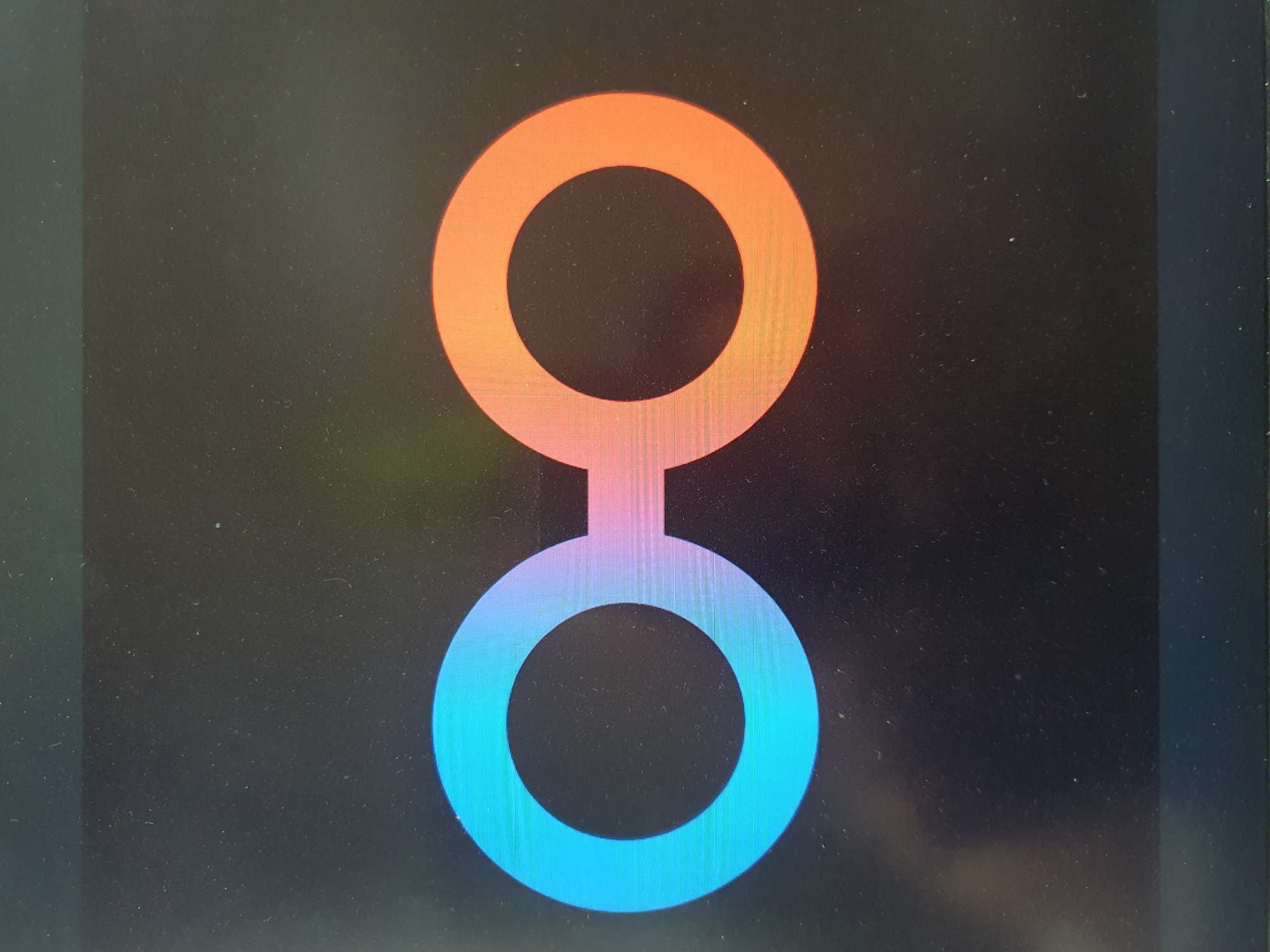 The image shows a close-up of a screen displaying a logo. The logo consists of two interconnected circles, with a gradient from blue to purple in the left circle and a gradient from pink to orange in the right circle. The circles are joined by a horizontal bar. The background is black, with visible dust particles on the screen. There is no indication of the location in Tashkent, Uzbekistan, or any other specific geographical context. The image is purely a visual representation of a digital graphic.