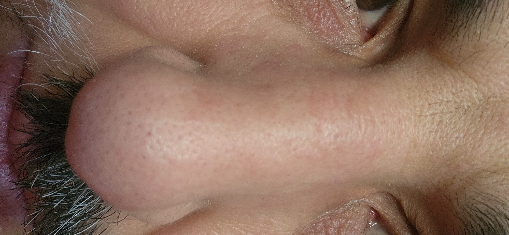 The image presents a close-up, inverted view of a human face, specifically the area around the nose, eyes, and mouth. The individual appears to have skin with visible pores and fine lines. There are grey and dark eyelashes. The image is not located in Norwich, United Kingdom. It is a studio image, not an outdoor scene.