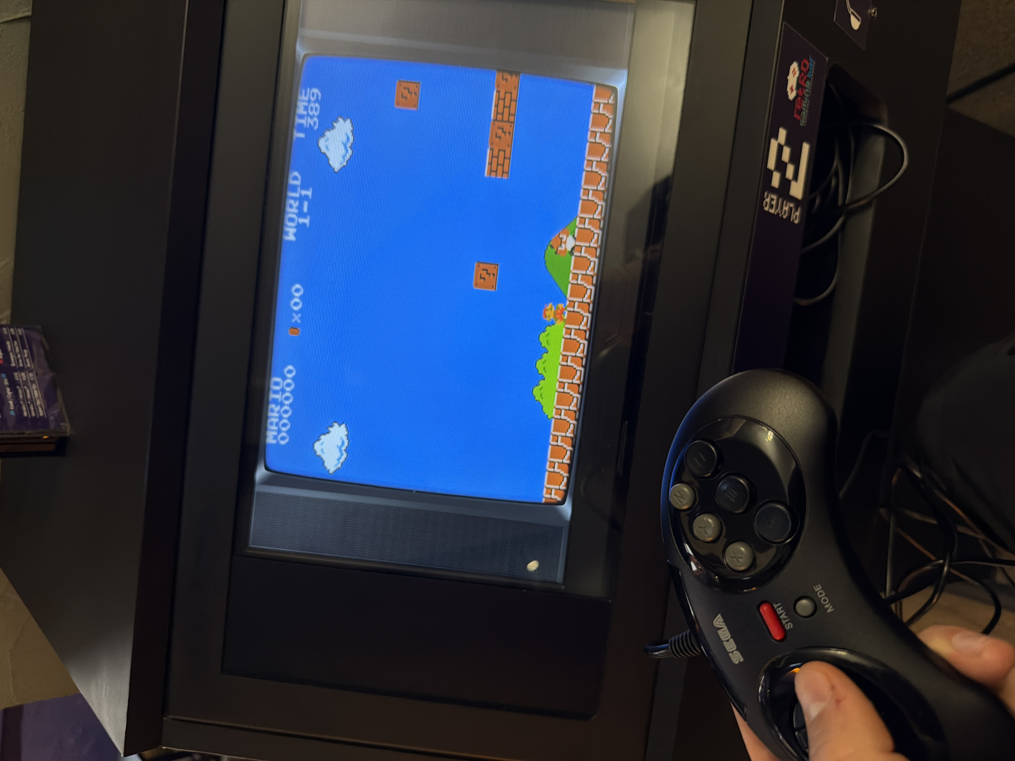 The image shows a person playing Super Mario Bros. on a CRT television. The person is holding a black Sega Genesis controller and pressing the right directional button. The game is on World 1-1. The setup appears to be part of an arcade console. Based on the presence of the "Retro Arena Player 2" label, it is likely the location is in Sofia, Bulgaria, where Retro Arena has several locations.