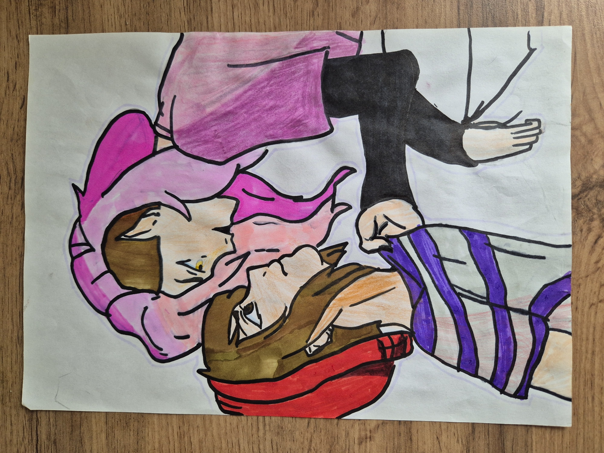 The image shows a colored drawing of two people. One figure, dressed in a pink shirt and black pants, is positioned at the top of the image. They have pink hair and are facing downwards. The other figure, wearing a red headband and a striped shirt with purple lines, is positioned at the bottom of the image, looking upwards. The drawing is on a white sheet of paper placed on a wooden surface.