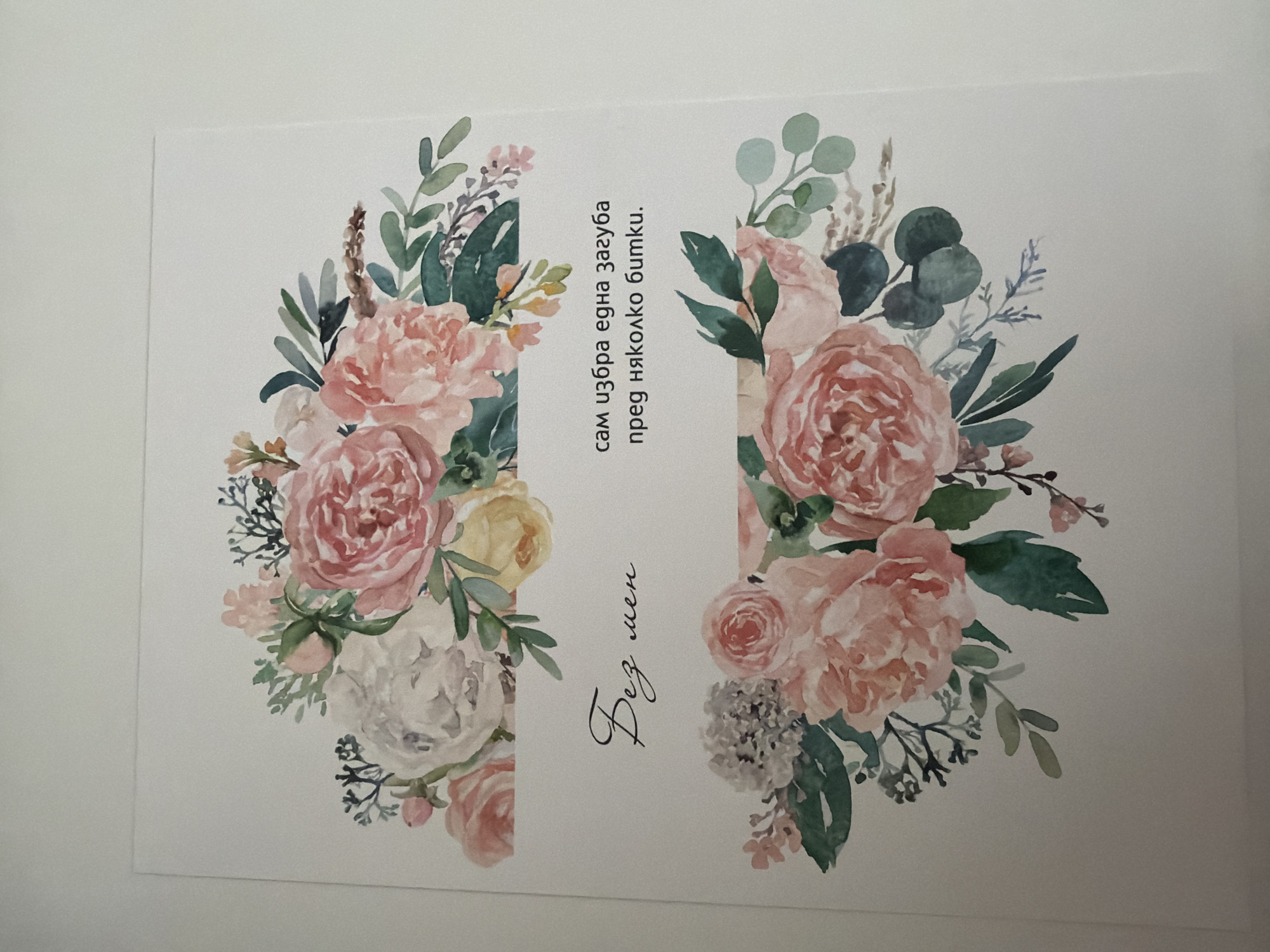 The image displays a card with a floral watercolor design. The top and bottom portions of the card feature bouquets of pink, white, and yellow roses with green foliage. In the center of the card, there are two lines of text in Bulgarian. The first line, in a decorative script, reads "Без мен" (Bez men), which translates to "Without me." The second line, in a standard font, reads "сам избра една загуба пред няколко битки." (sam izbra edna zaguba pred nyakolko bitki.), translating to "I chose one loss over several battles." The card is placed on a plain, light-colored surface, likely a table or desk, against a white wall. There are no discernible elements that suggest a specific location within the city of Pazardzhik, Bulgaria, or any interaction with people or a larger environment.