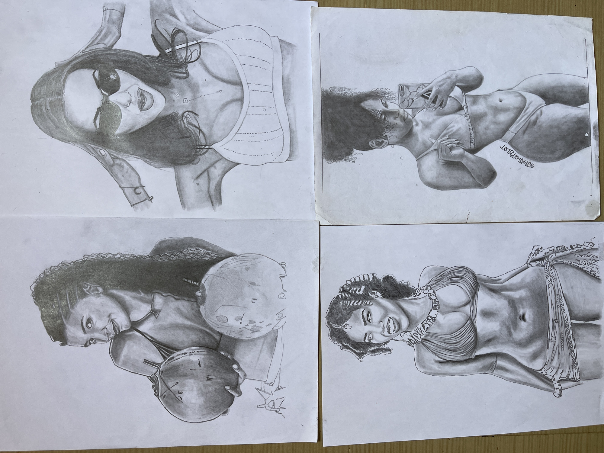 Four individual pencil drawings on white paper are arranged on a light brown surface.
Top left: A woman with sunglasses and dark hair is drawn from a low angle. She is wearing a top with visible straps. A bracelet is visible on her arm.
Top right: A woman with curly hair is lying down and taking a selfie with a mobile phone. She is wearing a bikini. A signature "OF THE PILOT" is visible.
Bottom left: A woman with long, curly hair is holding two globes with drawn lines. She has a necklace on. There are some scribbles on the paper near the bottom of the image.
Bottom right: A woman with curly hair is wearing a necklace, top, and a draped piece of material. She is smiling.
There are no visual indicators to verify that the location is in the city of Jos, Nigeria.