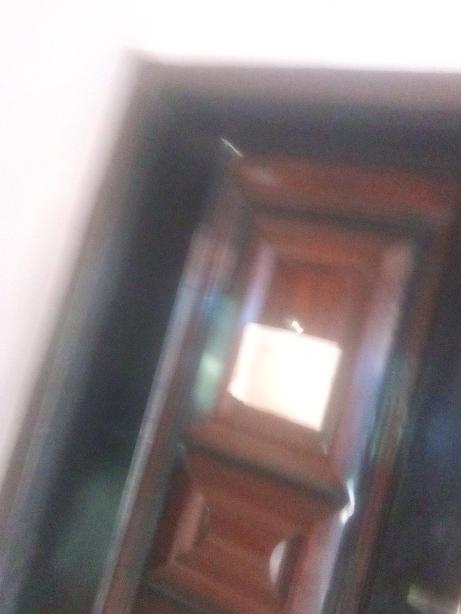 The media file is a slightly blurred, low-light, indoor photograph. The primary subject appears to be a dark brown wooden door with decorative paneling. A white piece of paper or label is affixed to the upper portion of the door. The lighting suggests an interior setting, possibly a hallway or room, with a lighter wall on the left side of the frame. The overall impression is dim and somewhat indistinct due to the blur and lighting conditions. No people are visible in the frame. The scene is static, with no discernible activity taking place. There are no clear indicators of the time of day or weather. The provided location context is Jalingo, Nigeria, but there are no specific visual cues within the image to confirm this location. No visible text other than the white paper on the door, which is illegible.