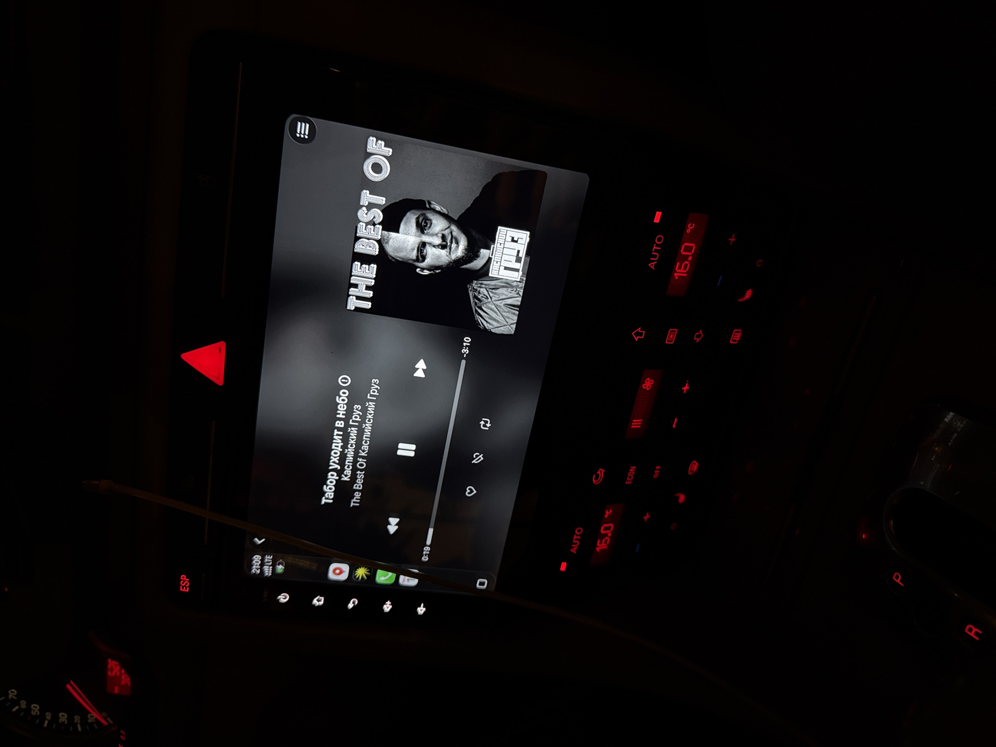 The image shows the interior of a car at night. The dashboard is visible, with a screen displaying a music track called "Табор уходит в небо" by "Каспийский Груз" from the album "The Best Of Каспийский Груз". The car's temperature is set to 16.0 degrees Celsius. The gear selector is visible, with "P" and "R" illuminated in red. Other indicators like "ESP" and hazard lights are also illuminated in red. The time is 21:09, and the phone signal is displayed as LTE.