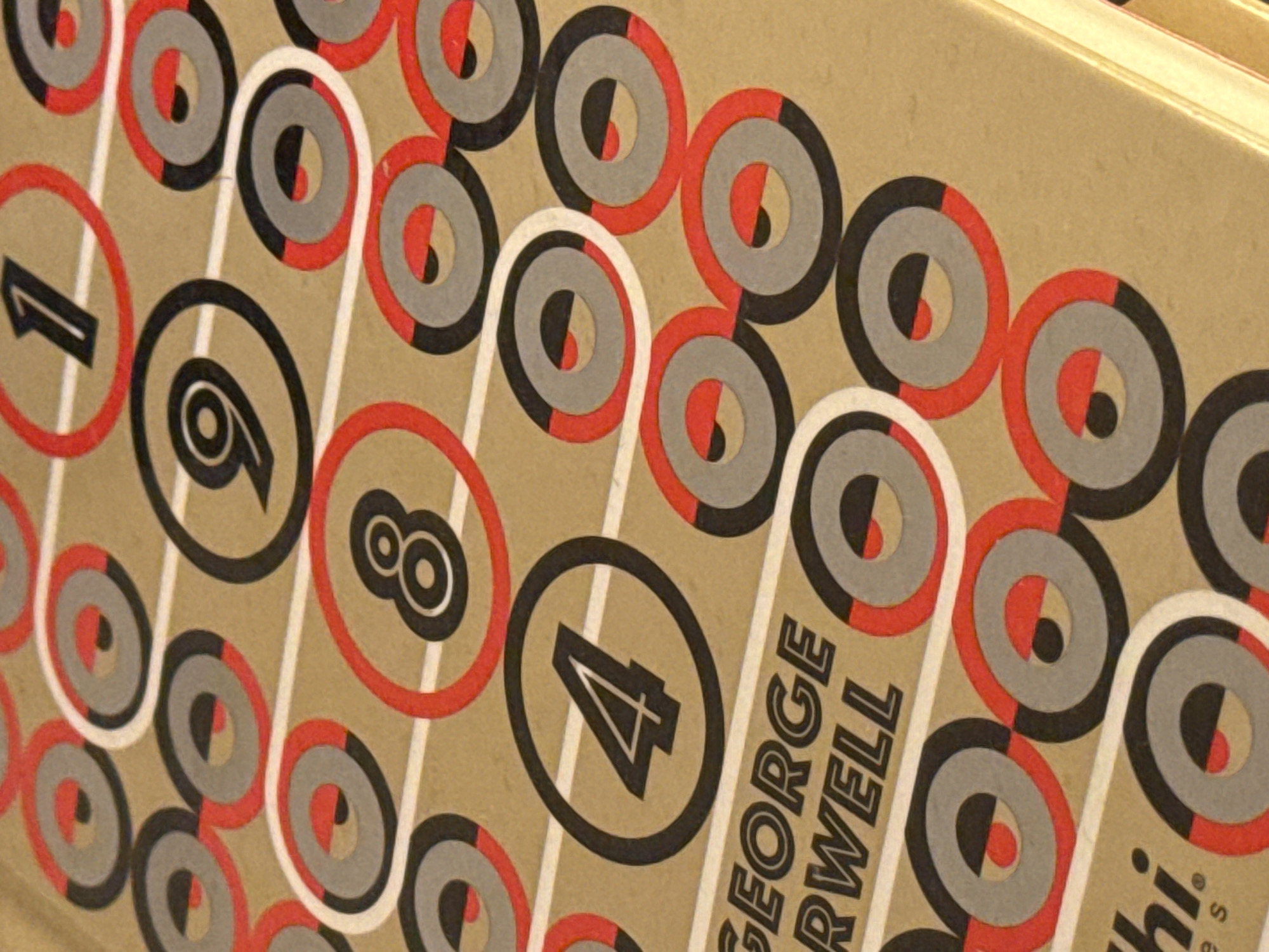 The image shows a close-up of a book cover with a geometric design. The design consists of circles in red, black, and gray on a tan background. Some of the circles contain numbers: 1, 6, 8, and 4. Part of the author's name, "GEORGE ORWELL," is visible. There is no indication of location in San Bernardino Tlaxcalancingo, Mexico, in the image.