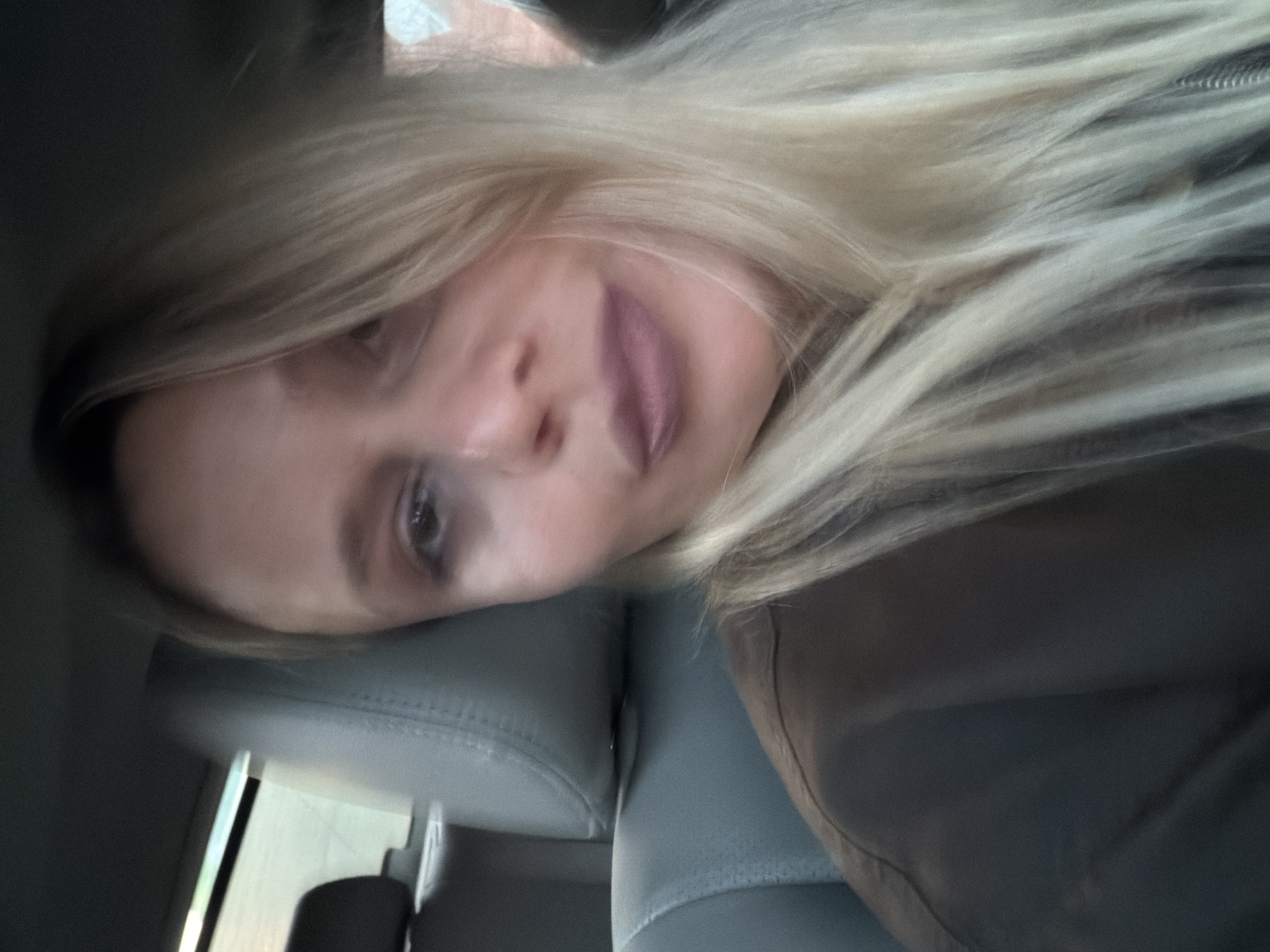 A woman with blonde hair is reclined in the driver's seat of a car. She is resting against the headrest, facing the camera. The interior of the car is visible, with a light-colored leather seat. The image does not provide enough information to determine the specific location in Sarapul, Russia.